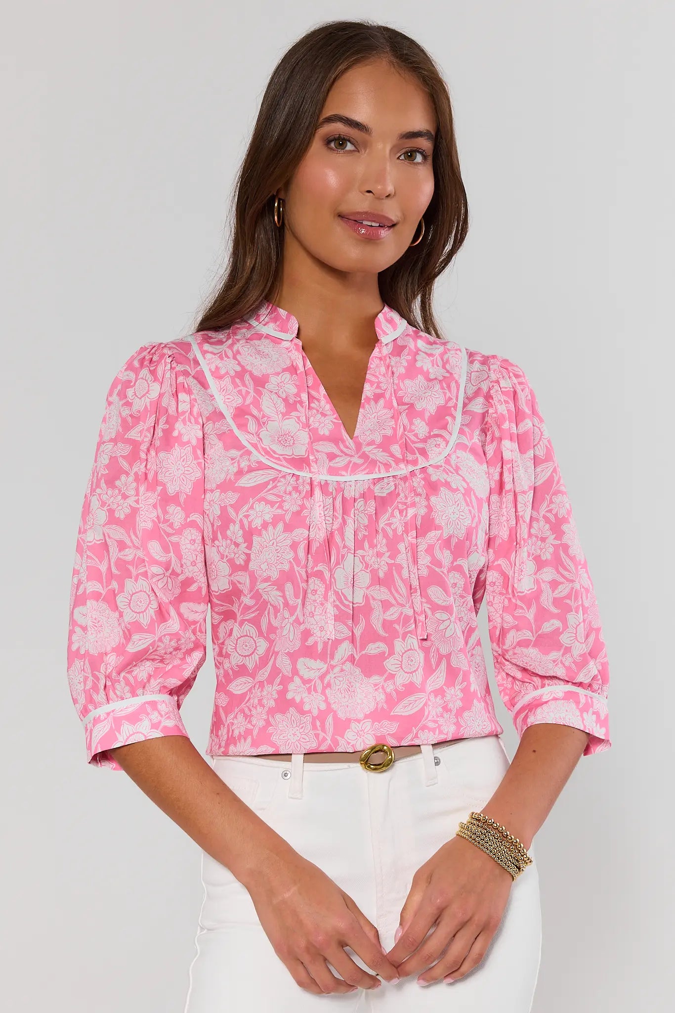 Woman wearing a pink floral blouse with white pants on a plain background