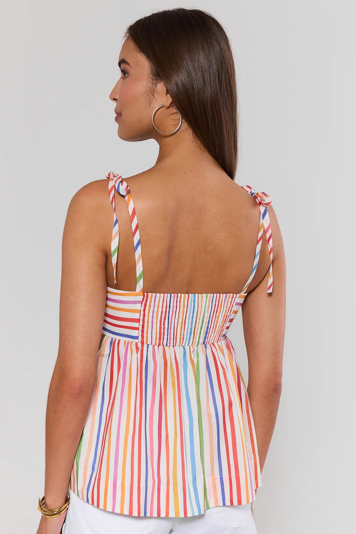 Woman standing wearing a colorful striped top with thin straps on a plain background