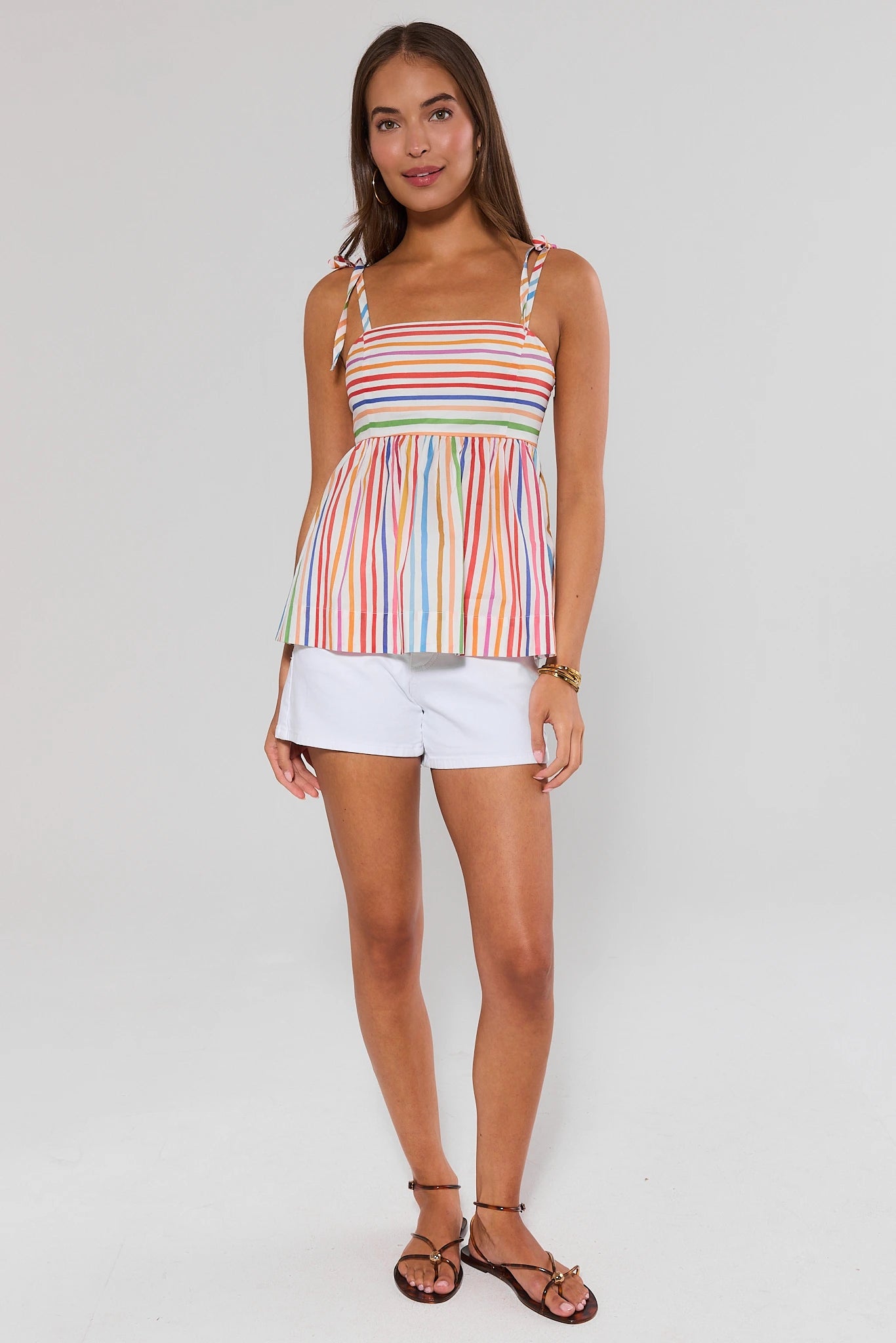 Woman wearing a colorful striped tank top and white shorts on a plain background