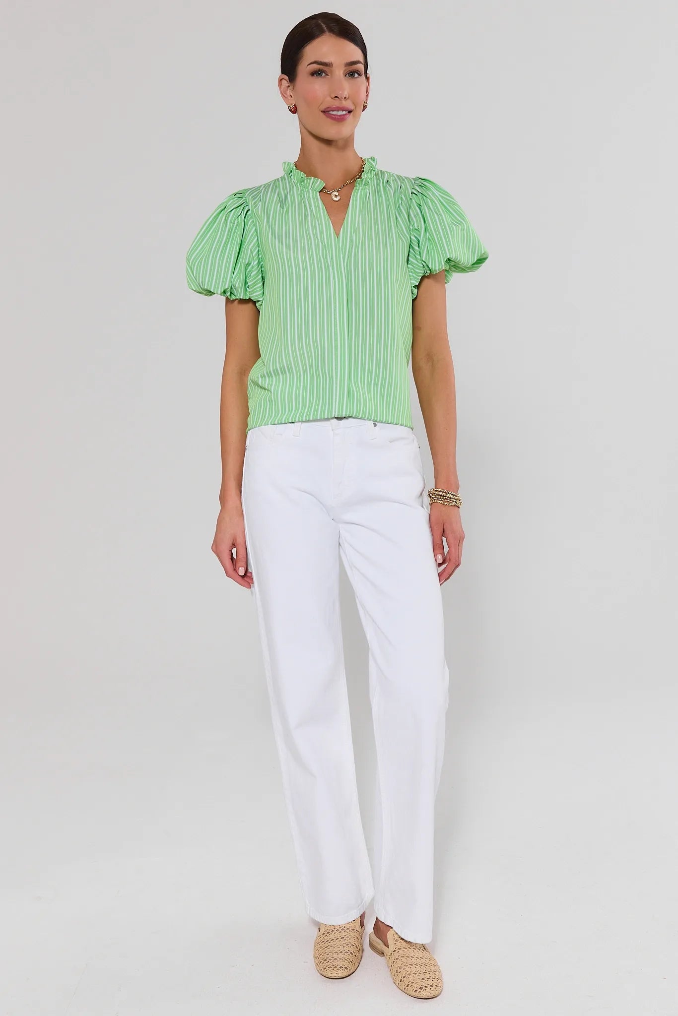 Woman wearing a ophelia green striped blouse and white pants on a plain background