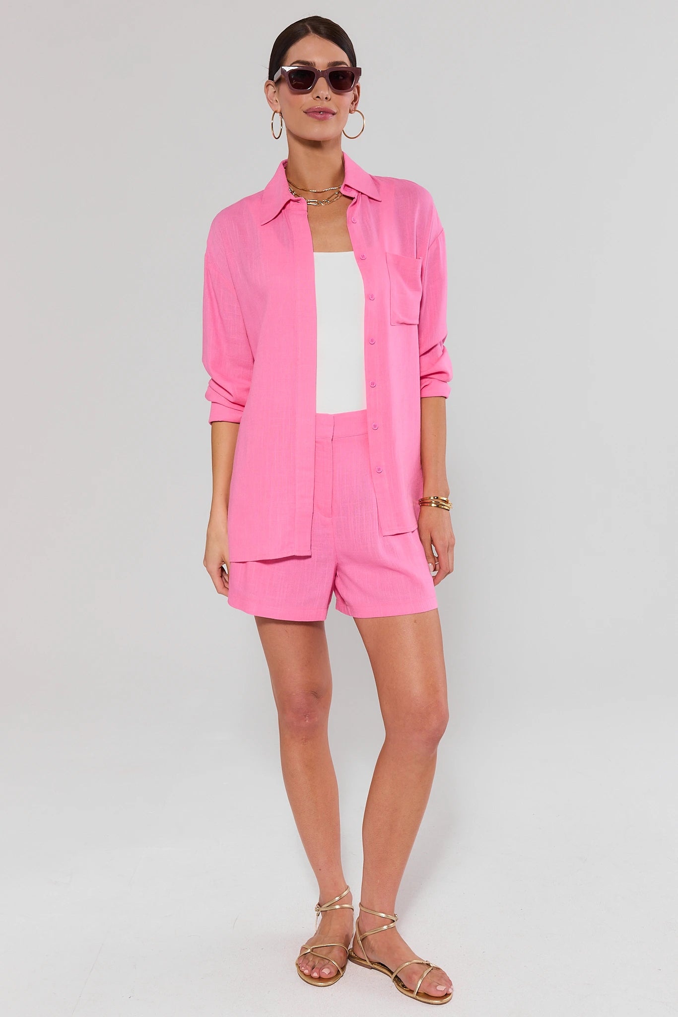 Woman wearing a pink outfit with sunglasses on a plain background