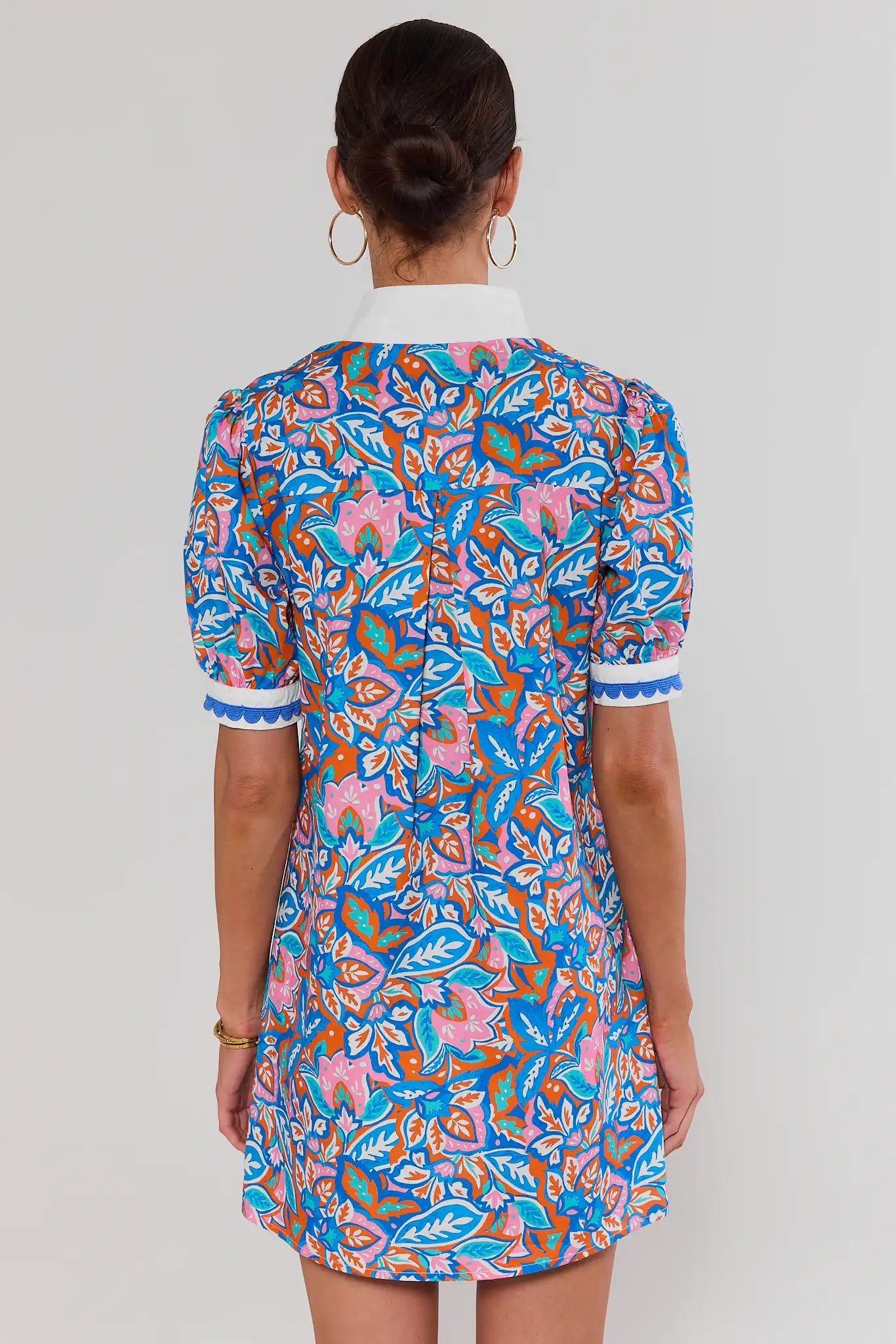 Woman standing wearing a colorful patterned dress against a plain background