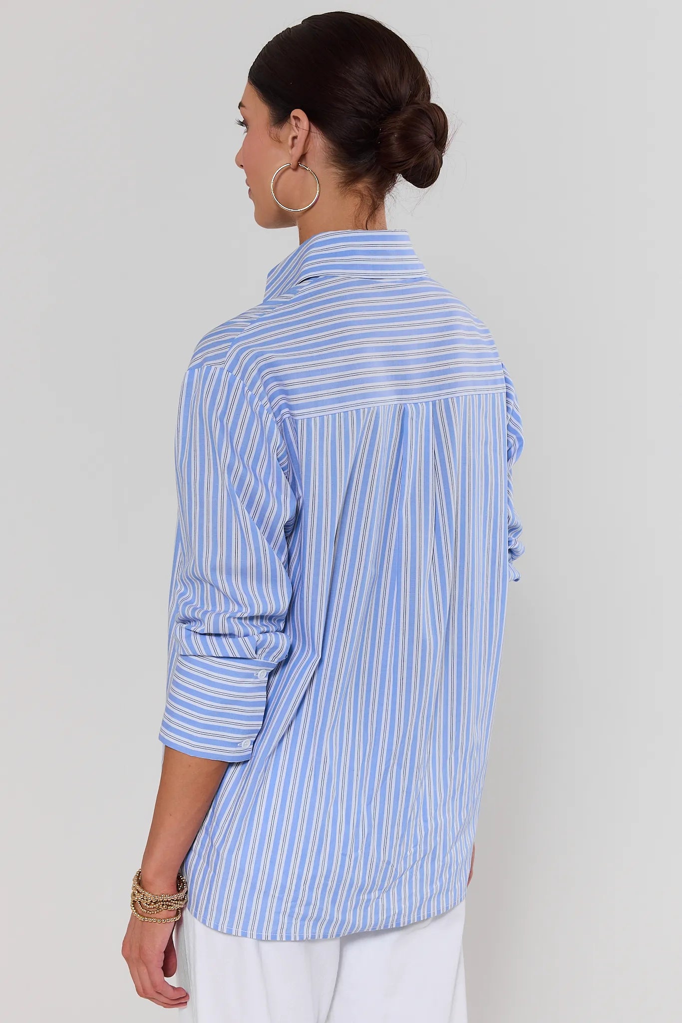 Woman standing wearing a blue and white striped shirt against a plain background