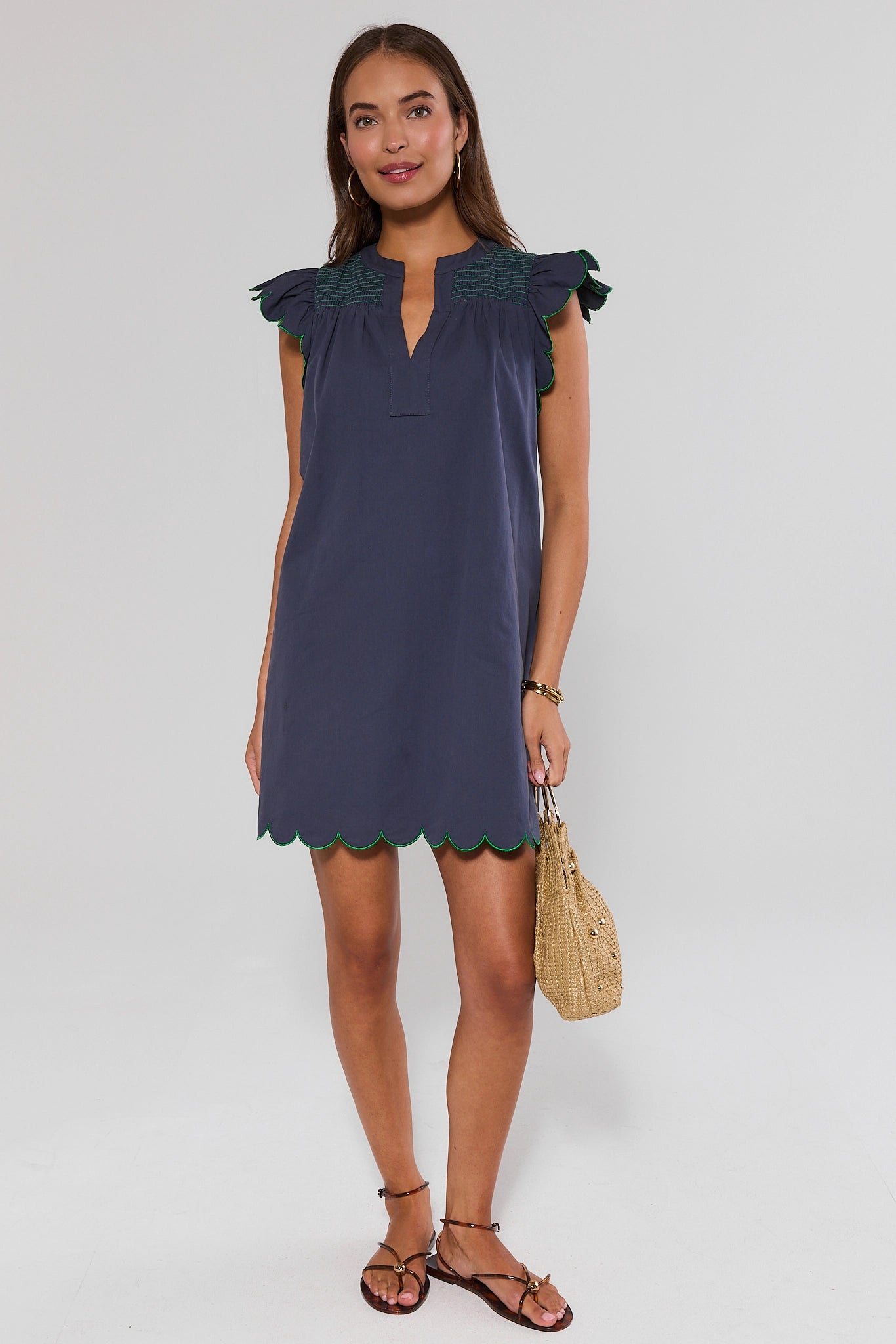 Woman standing wearing a navy dress with ruffled shoulders on a white background 