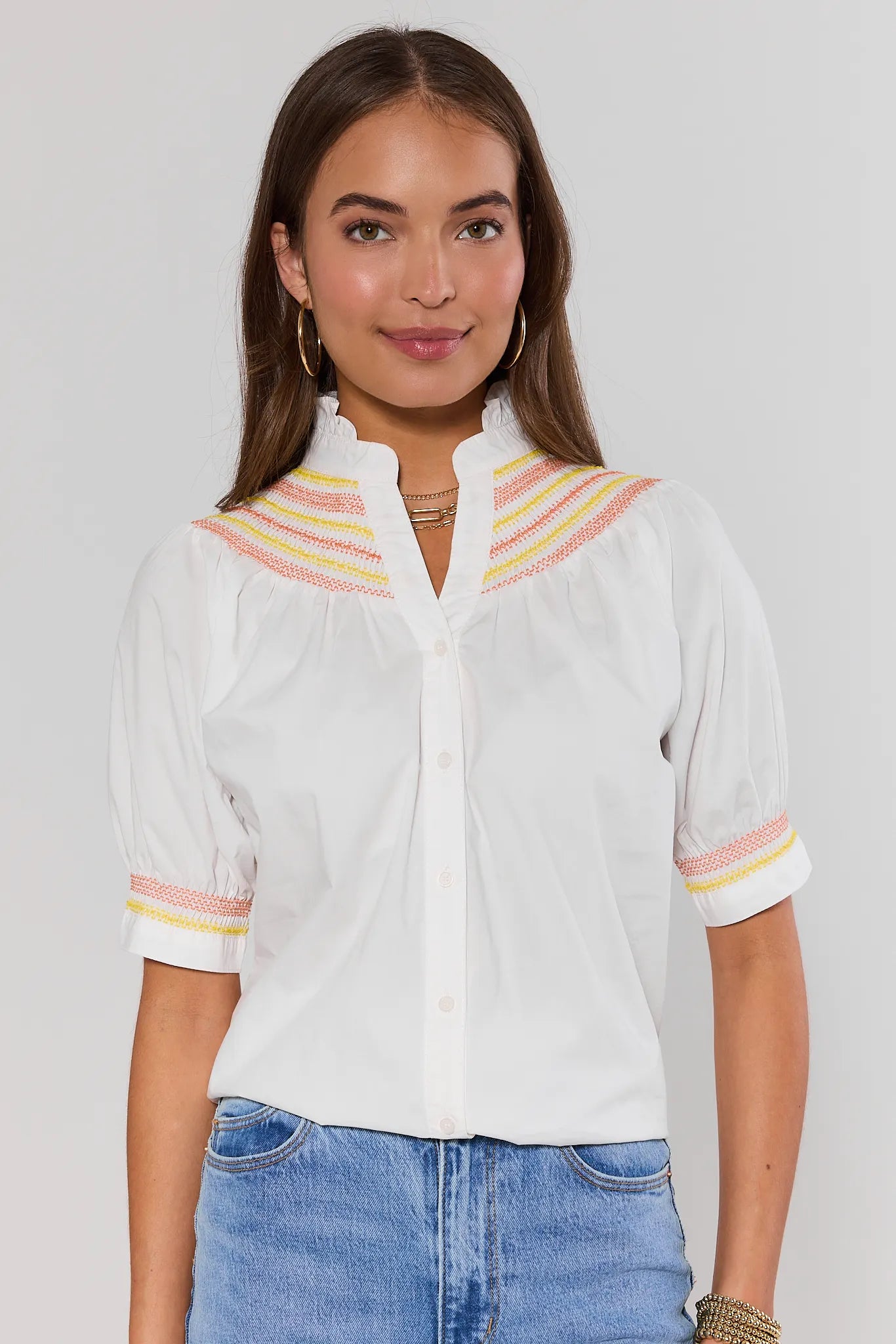 Woman wearing a white blouse with colorful accents on a plain background