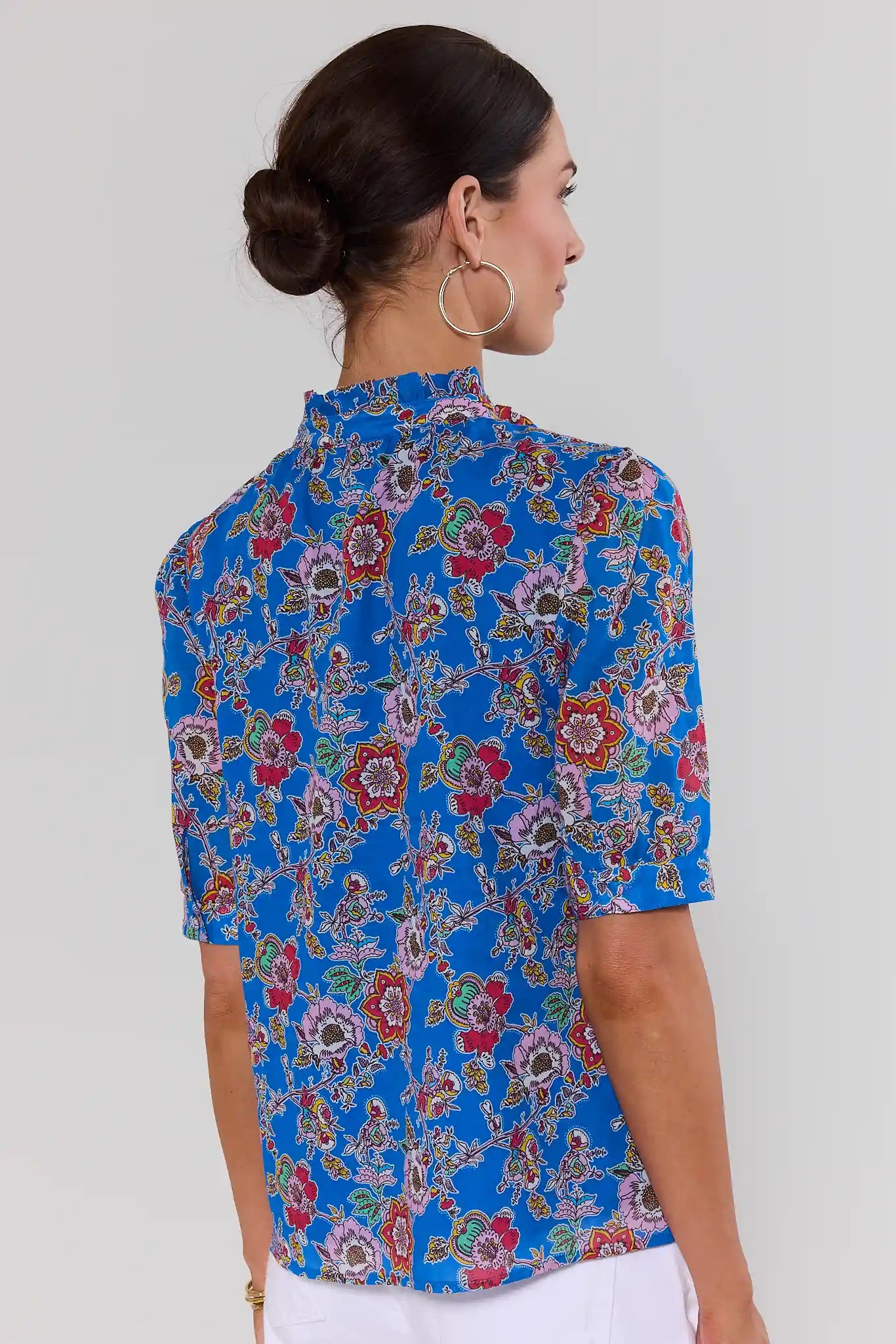 Woman wearing a blue floral patterned shirt against a white background standing 