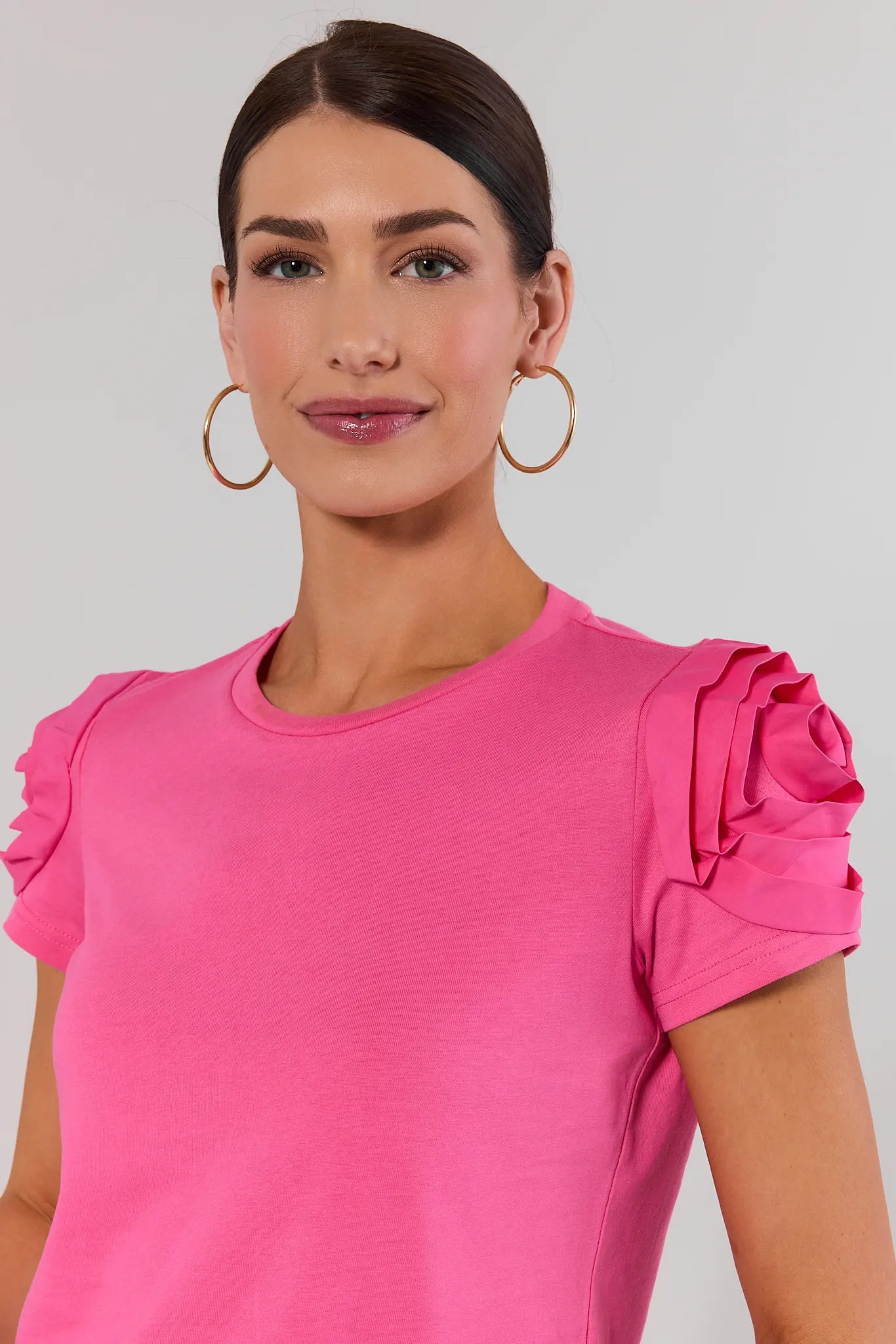 close up Woman wearing a pink top with ruffled sleeves against a plain background