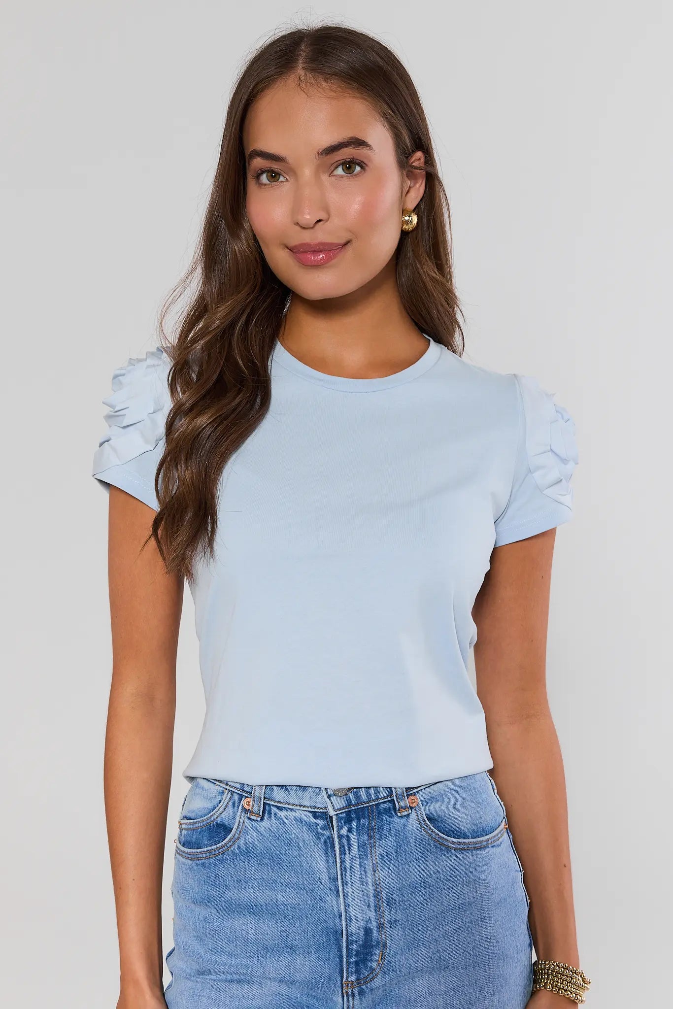 Woman wearing a light blue top with ruffled sleeves and jeans on a plain background