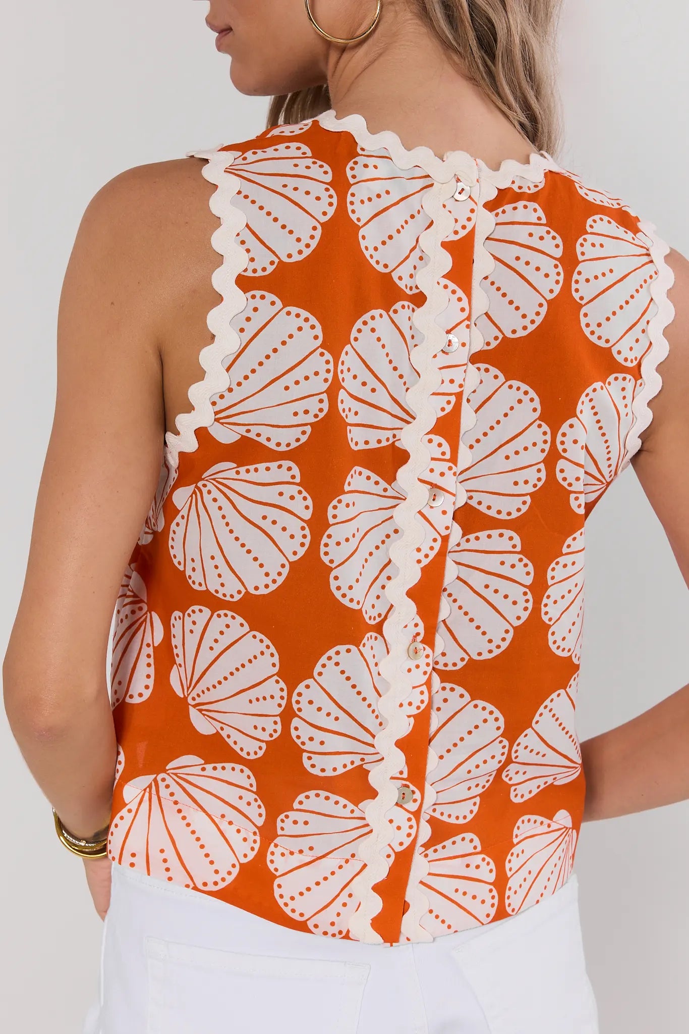 Orange sleeveless top with white shell pattern worn by a person on a plain background back