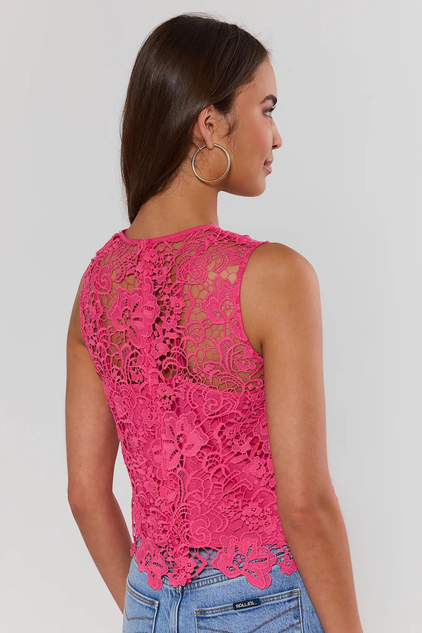 Woman wearing a pink lace top against a white background standing
