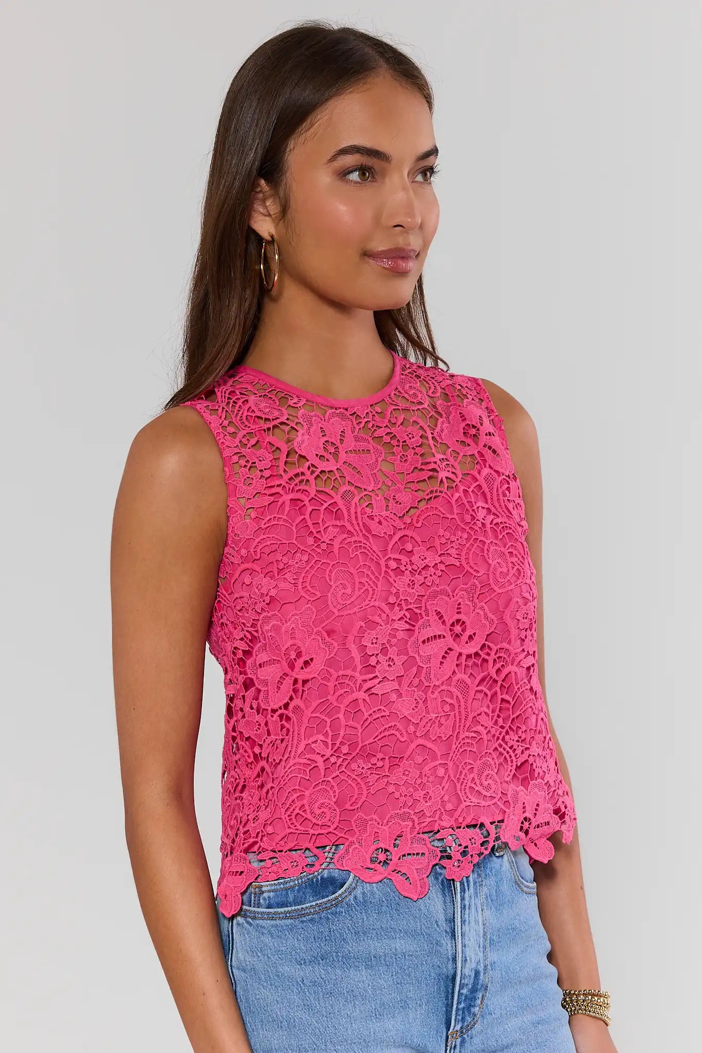 side shot Woman wearing a pink lace top and blue jeans on a plain background