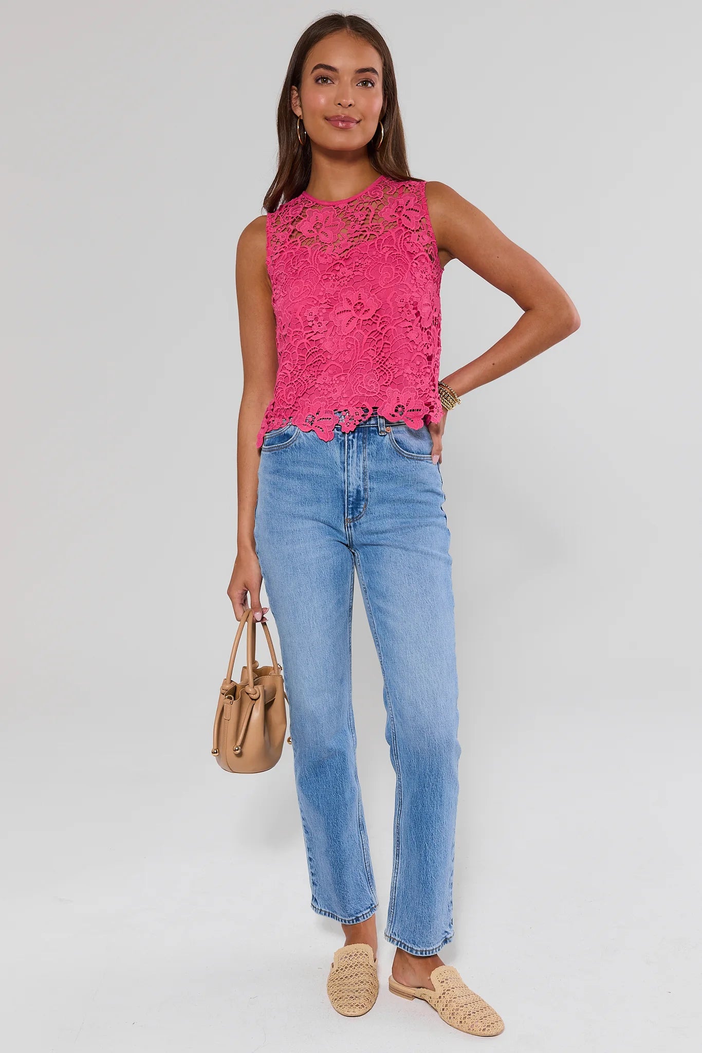 Woman wearing a pink lace top and blue jeans, standing against a white background