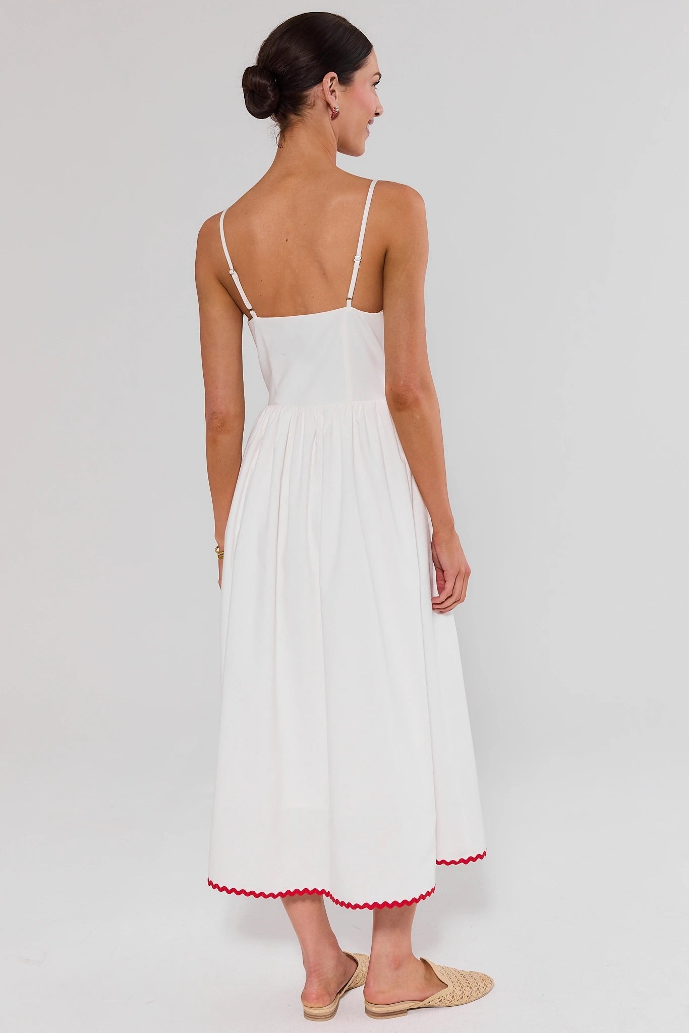 Woman standing wearing a white dress with red trim on a plain background