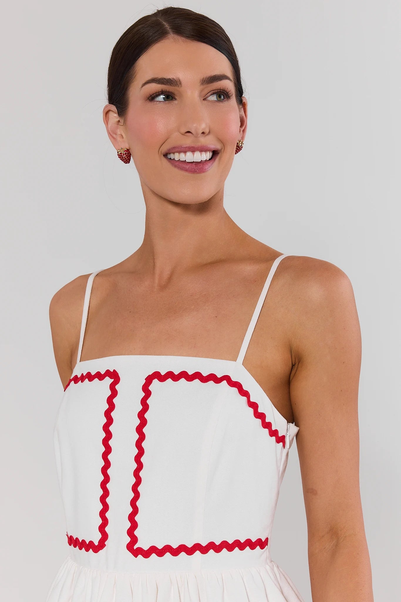 close up Woman wearing a white dress with red trim against a plain background
