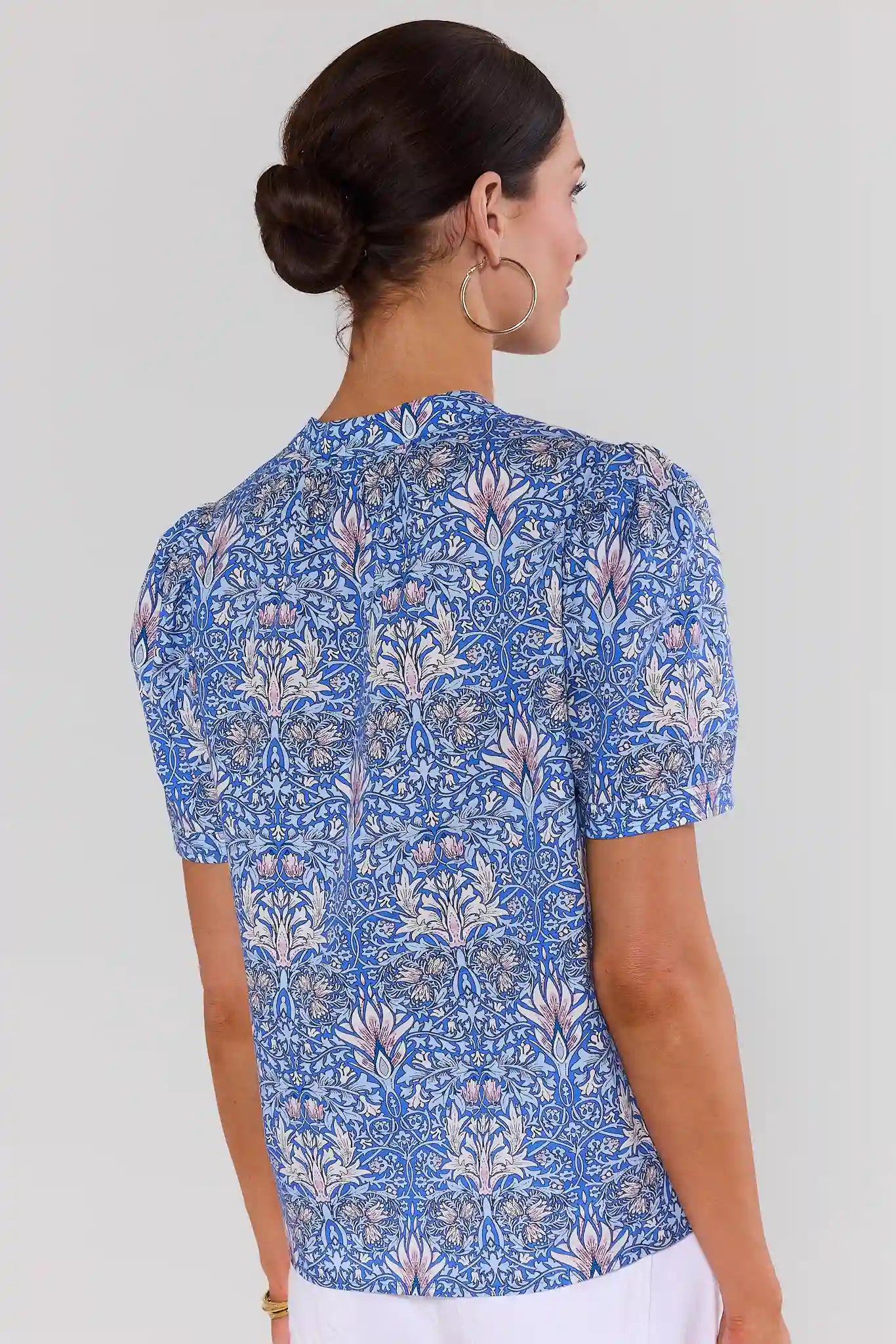 Woman standing wearing a blue floral patterned top on a plain background