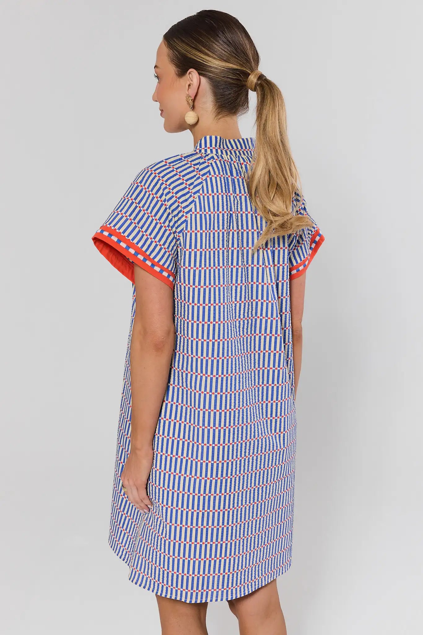Woman wearing a patterned dress with red trim on a plain background standing