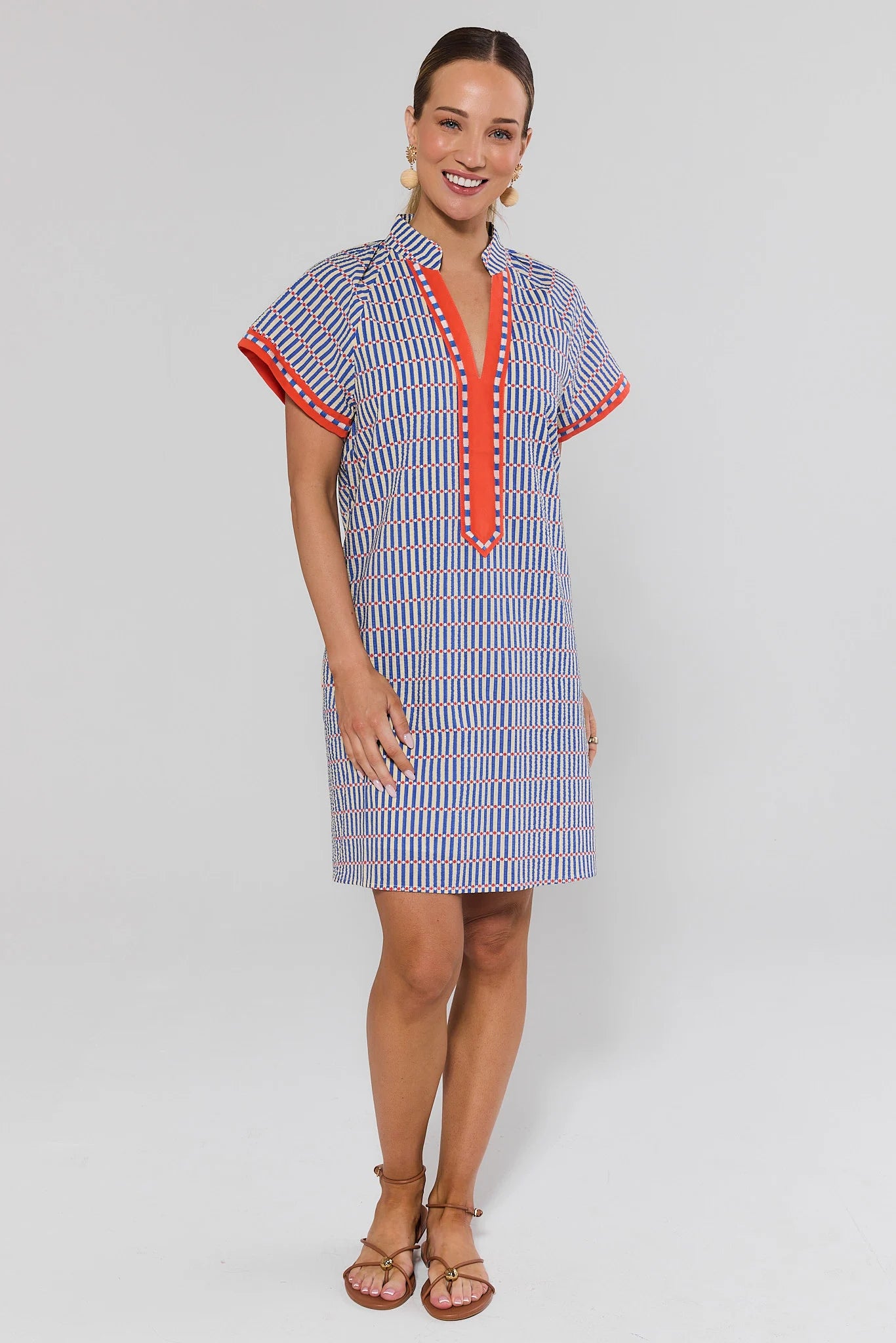 Woman standing wearing a blue and red striped dress with a white background