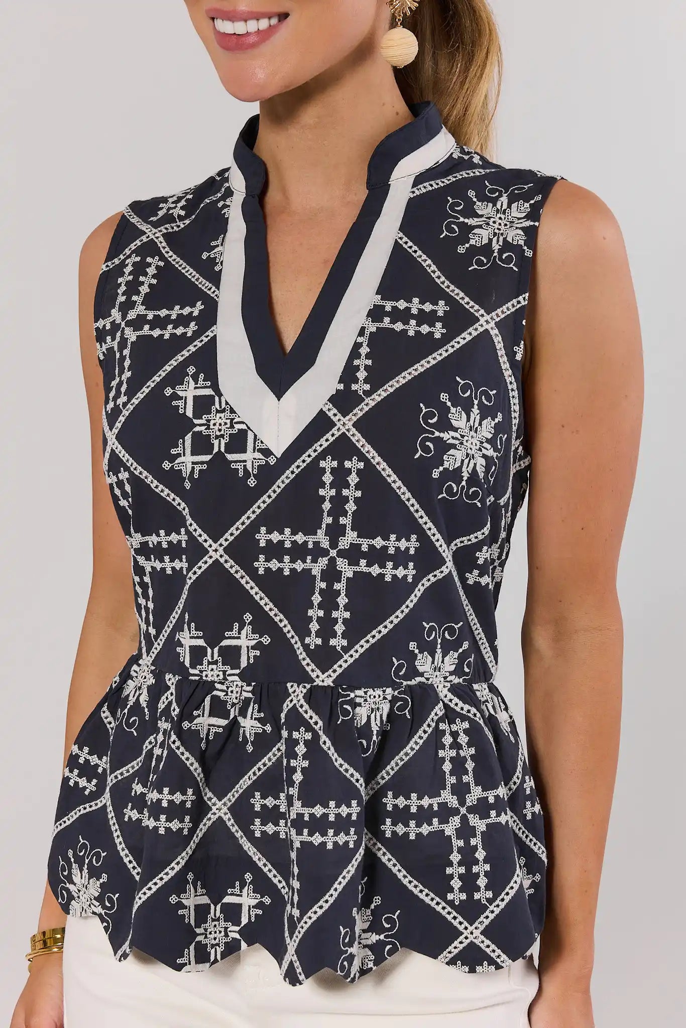 Woman wearing a navy blue sleeveless top with white geometric pattern on a plain background close up 