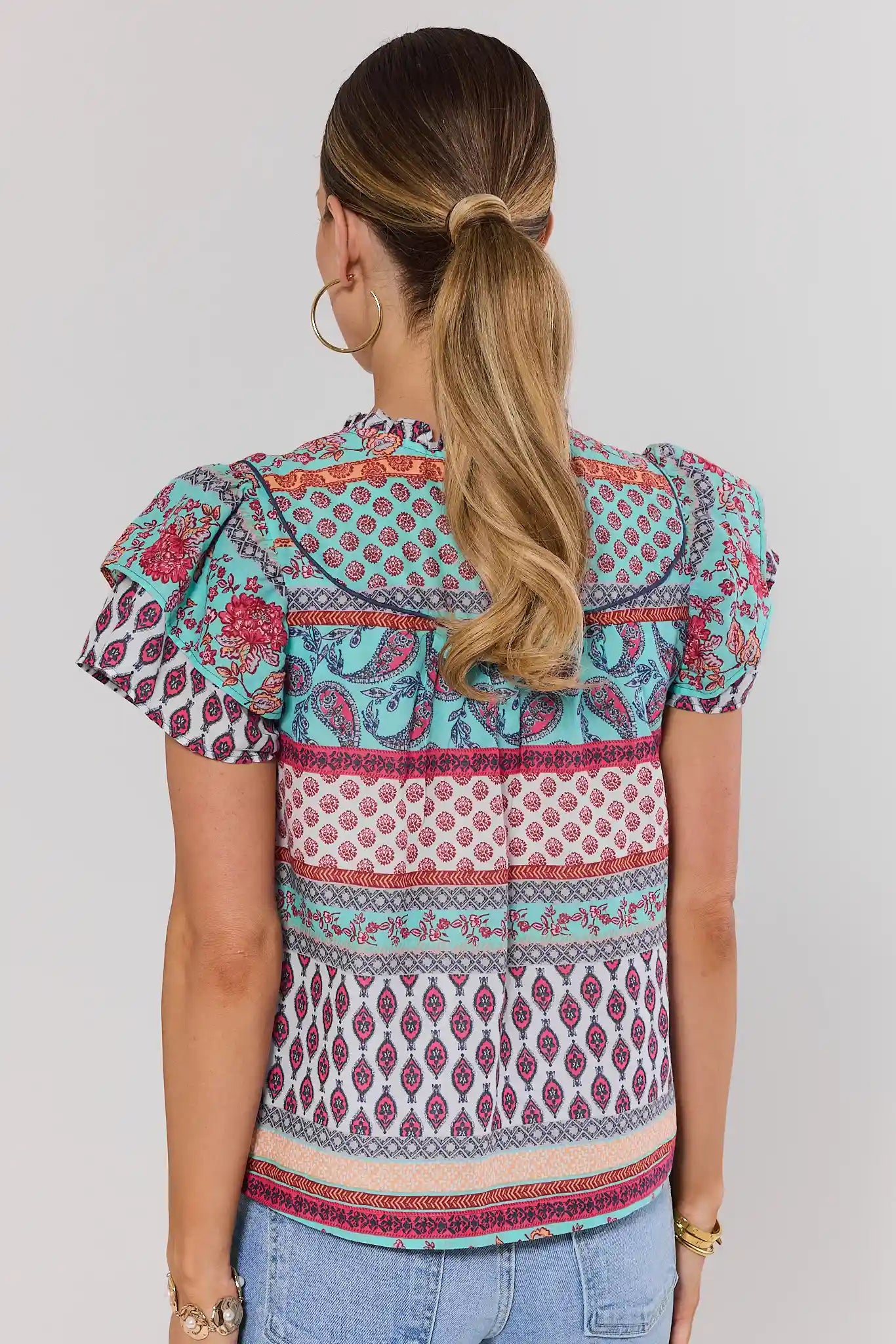 Woman standing wearing a colorful patterned blouse with short sleeves on a plain background