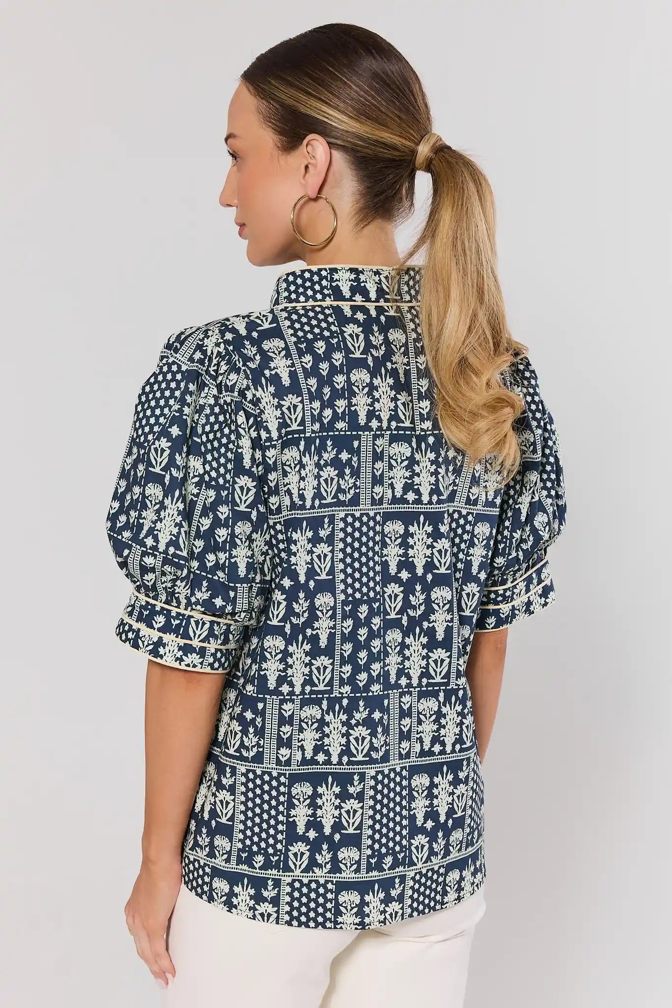 Woman standing wearing a navy patterned blouse against a white background