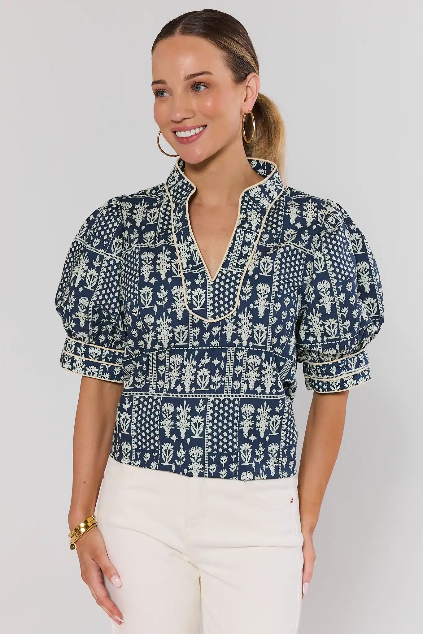 Woman wearing a navy patterned dakota blouse with white pants on a  background