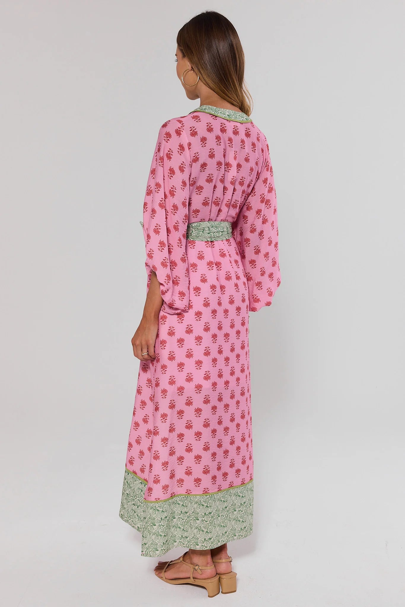 Woman standing wearing a pink and green dress with a background