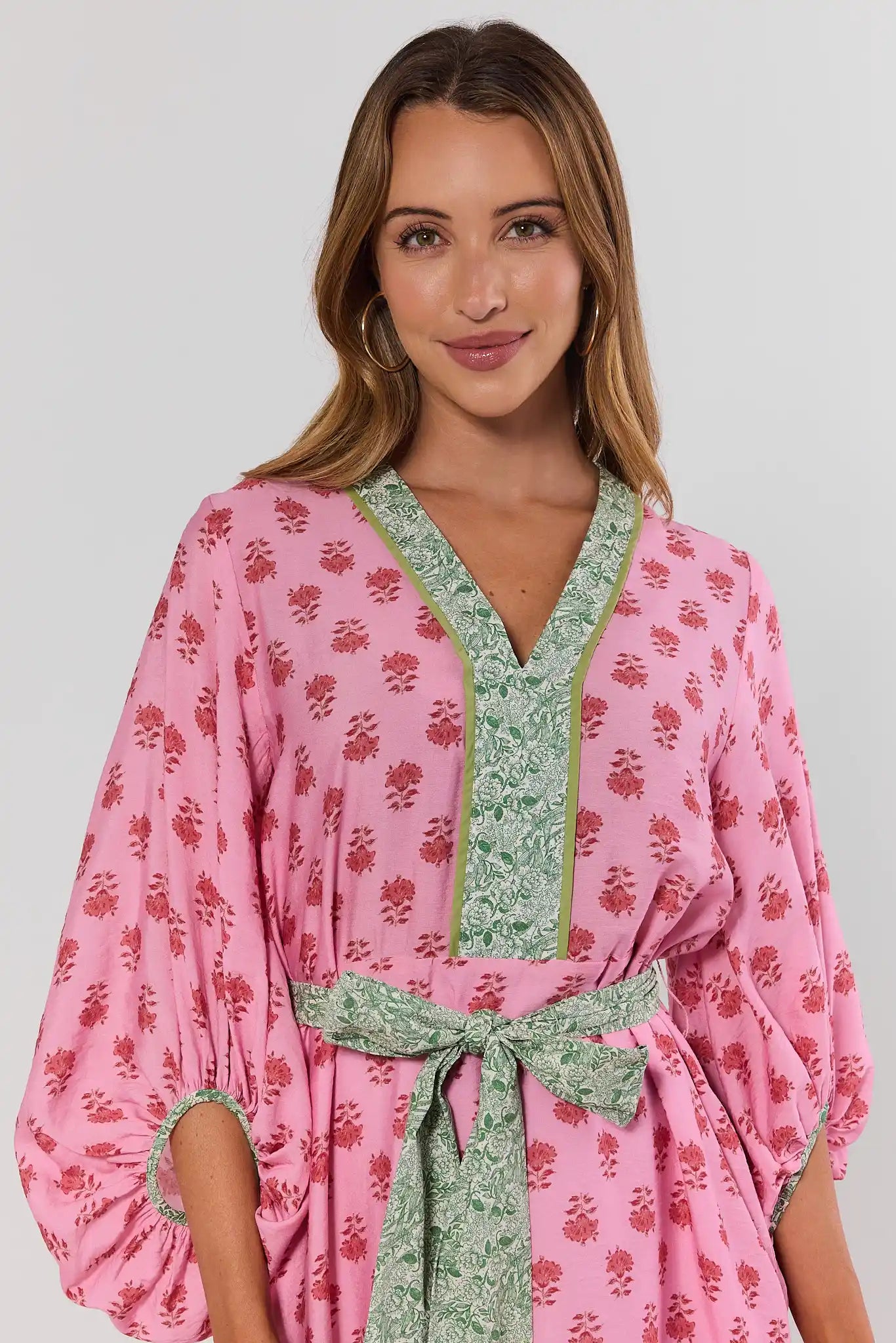 close up Woman wearing a pink floral dress with green trim on a plain background