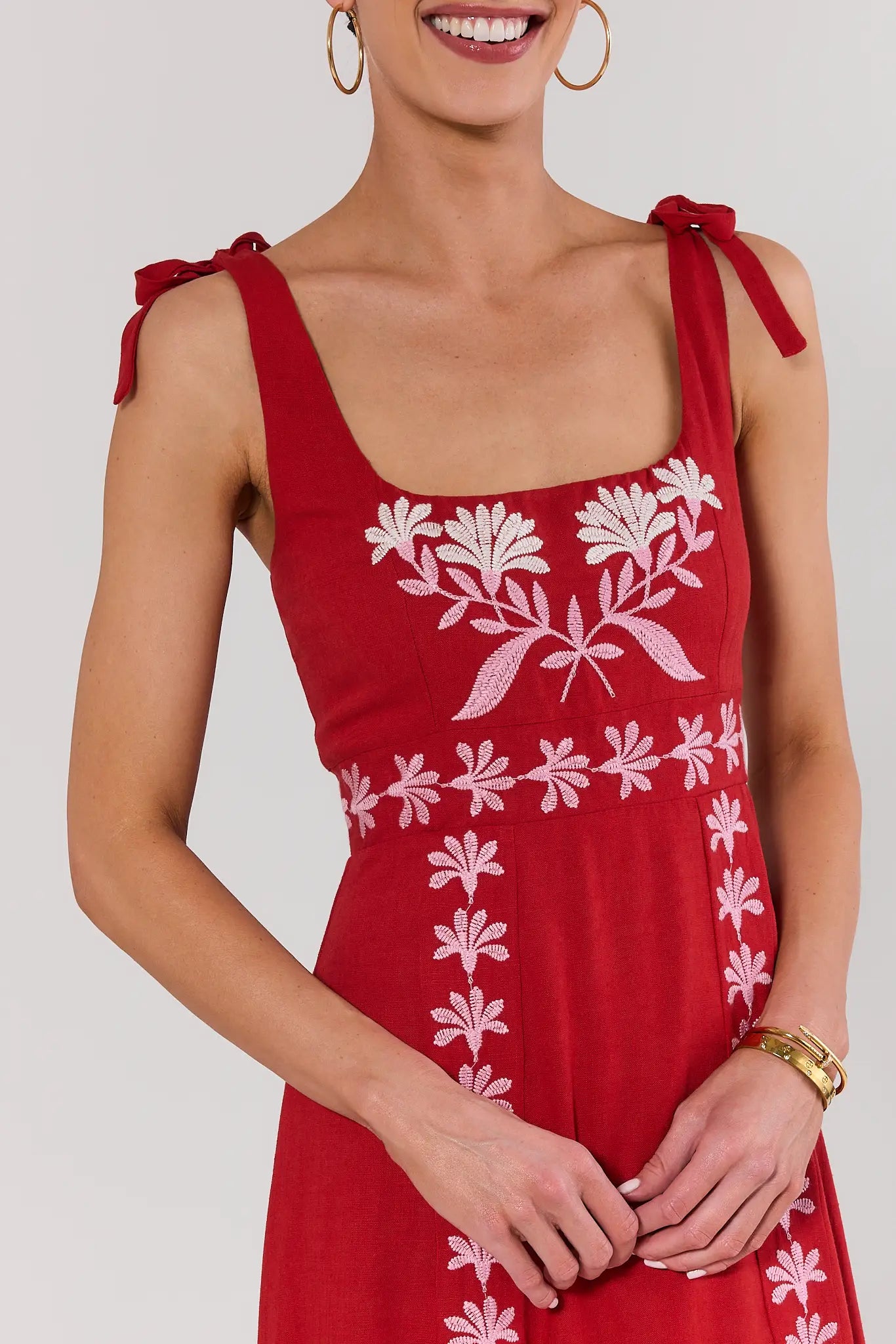 Woman standing wearing a red dress with white floral patterns on a plain background