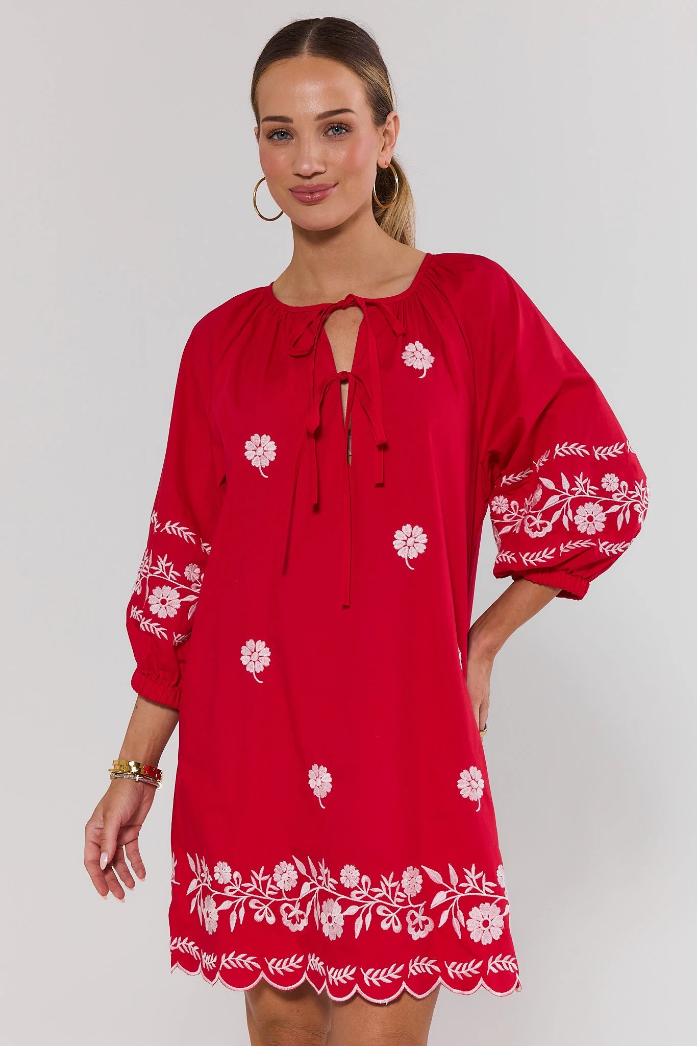 Woman wearing a red dress with white floral embroidery on a plain background