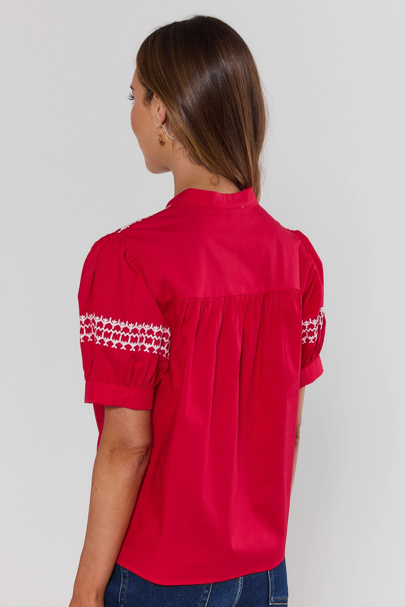 Red blouse with white embroidery on sleeves worn by a person on a plain background standing