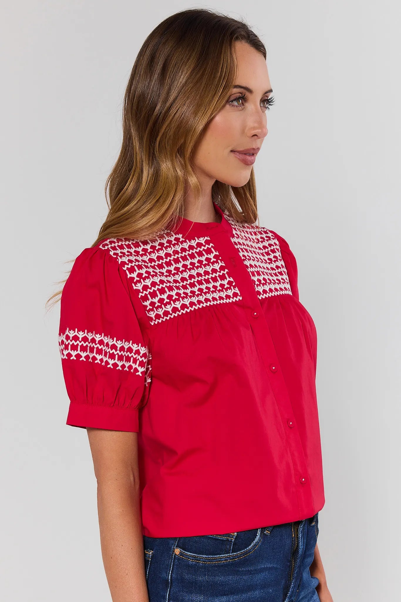 side shot Woman wearing a red blouse with white embroidery on a plain background