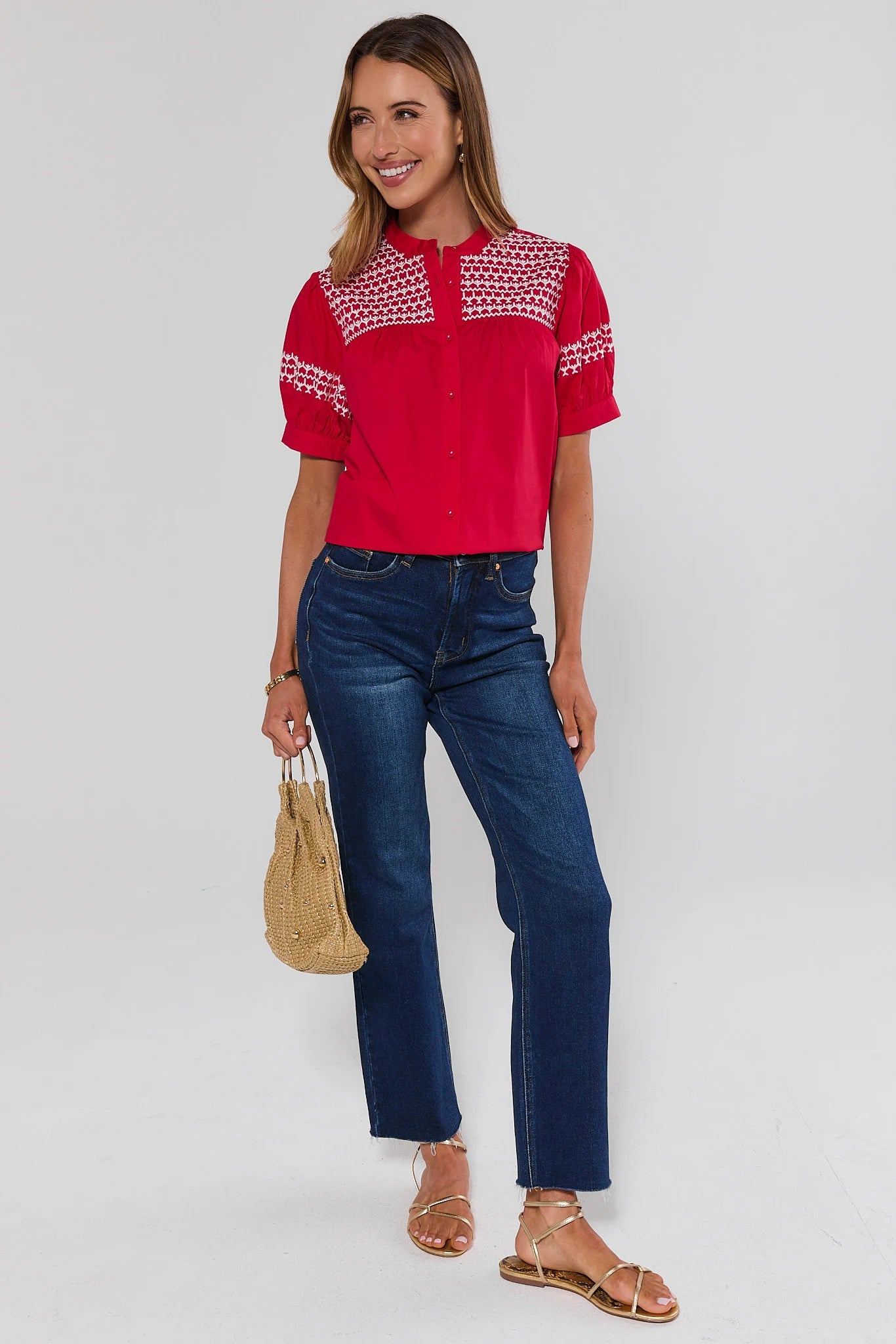 Woman wearing a red embroidered trudy blouse and blue jeans on a white background