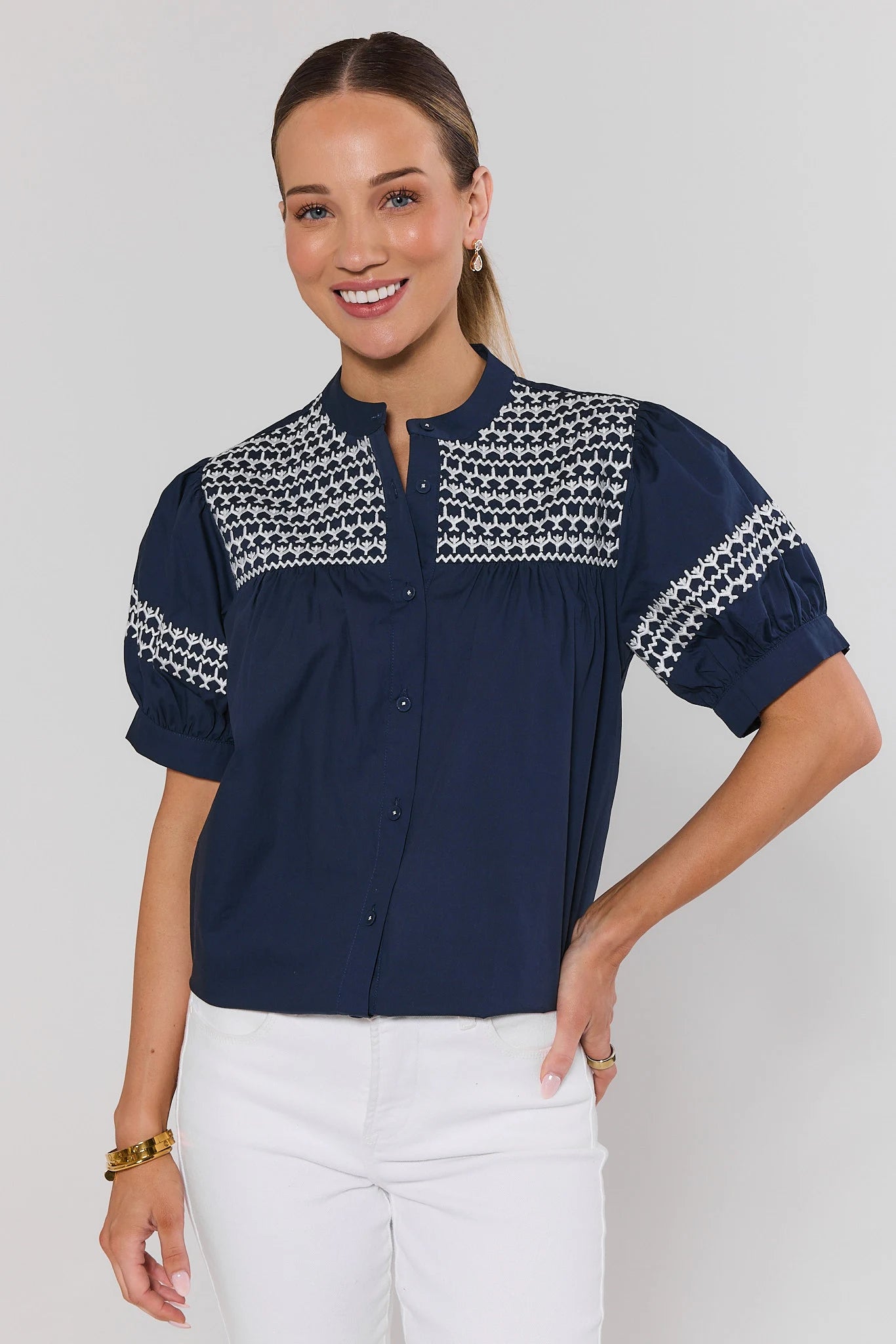 Woman wearing a navy blouse with white patterned accents on a plain background