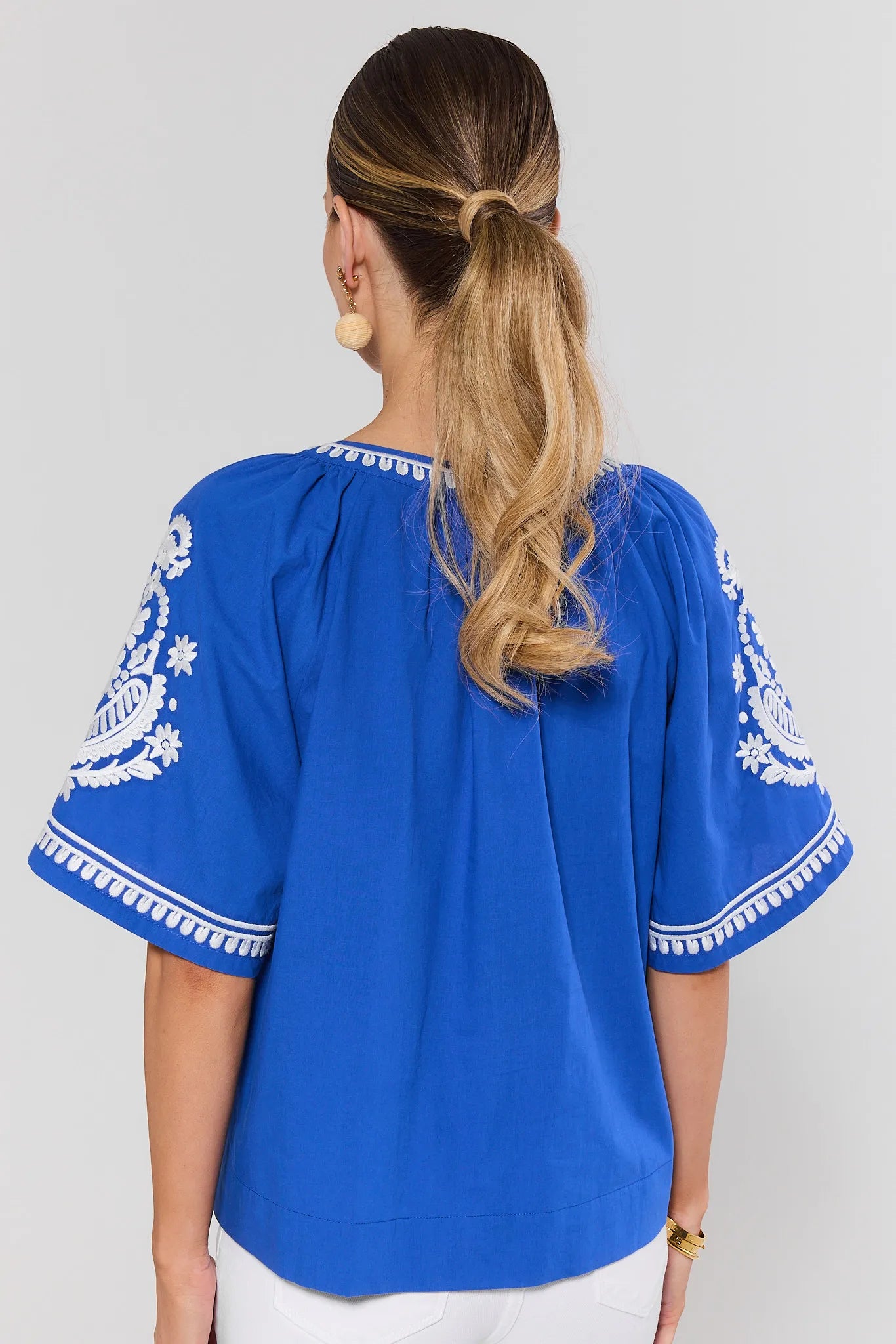 Woman wearing a blue blouse with white embroidery on a plain background standing