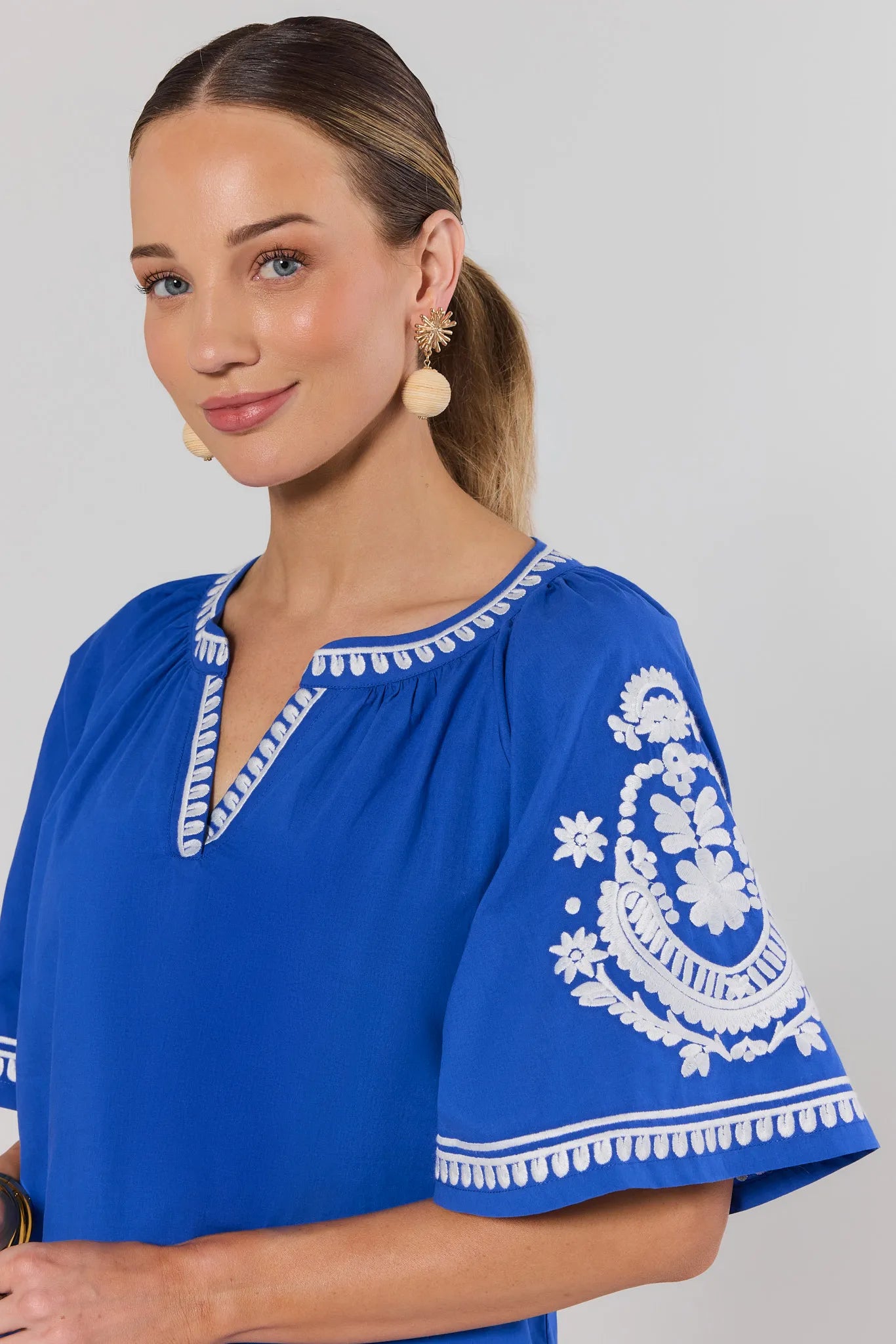 Woman wearing a blue top with white embroidery on a gray background close up