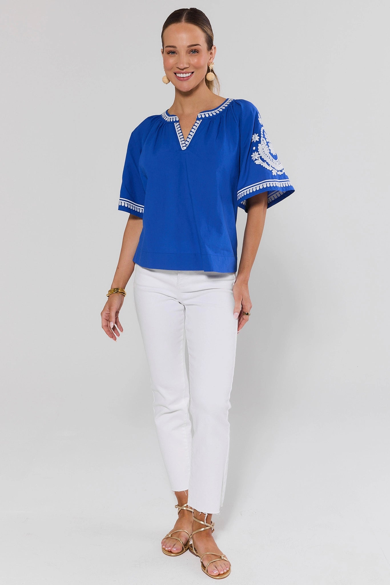 Woman standing wearing a blue top with white pants on a background