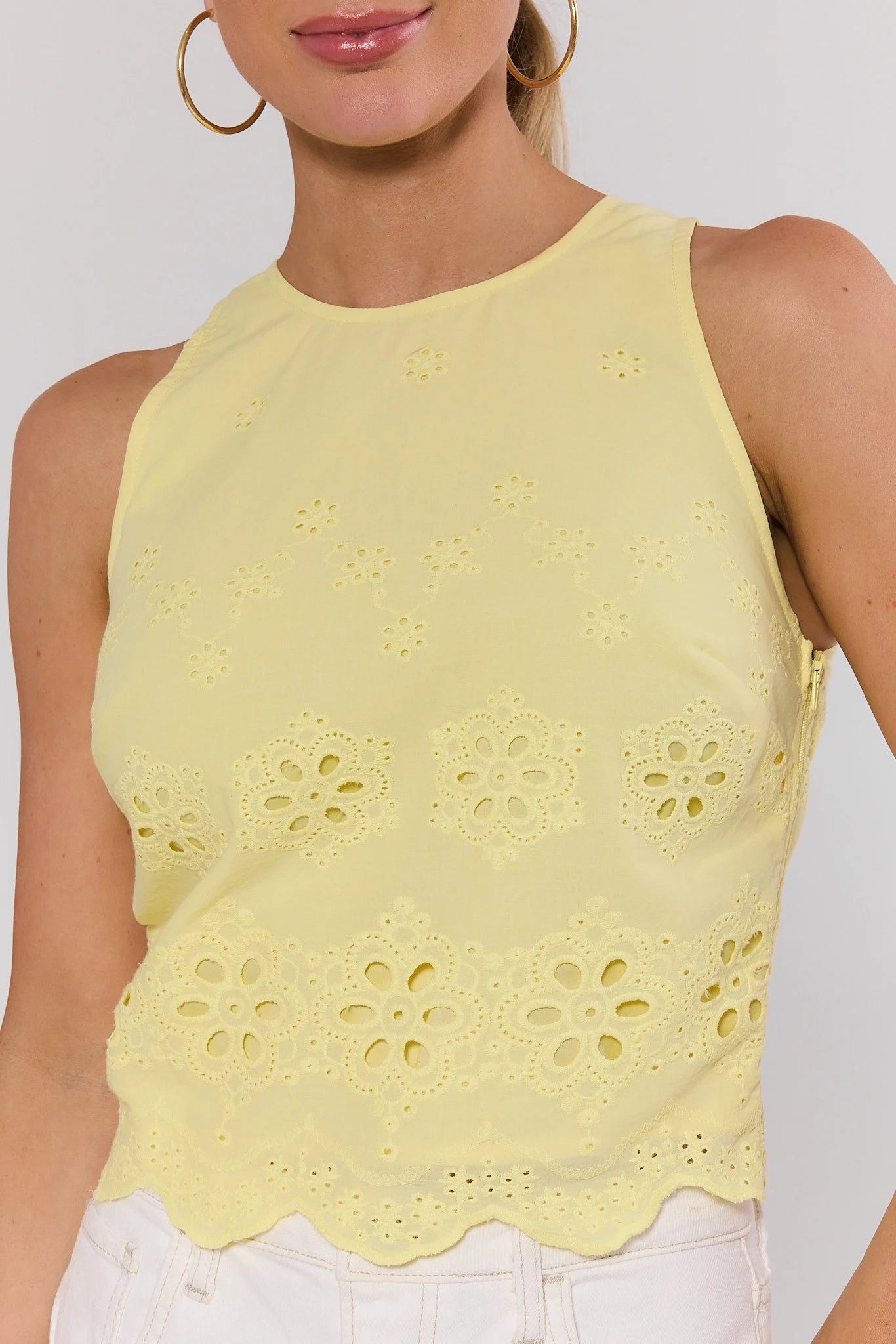 Yellow sleeveless top with floral cut-out design on a plain background close up