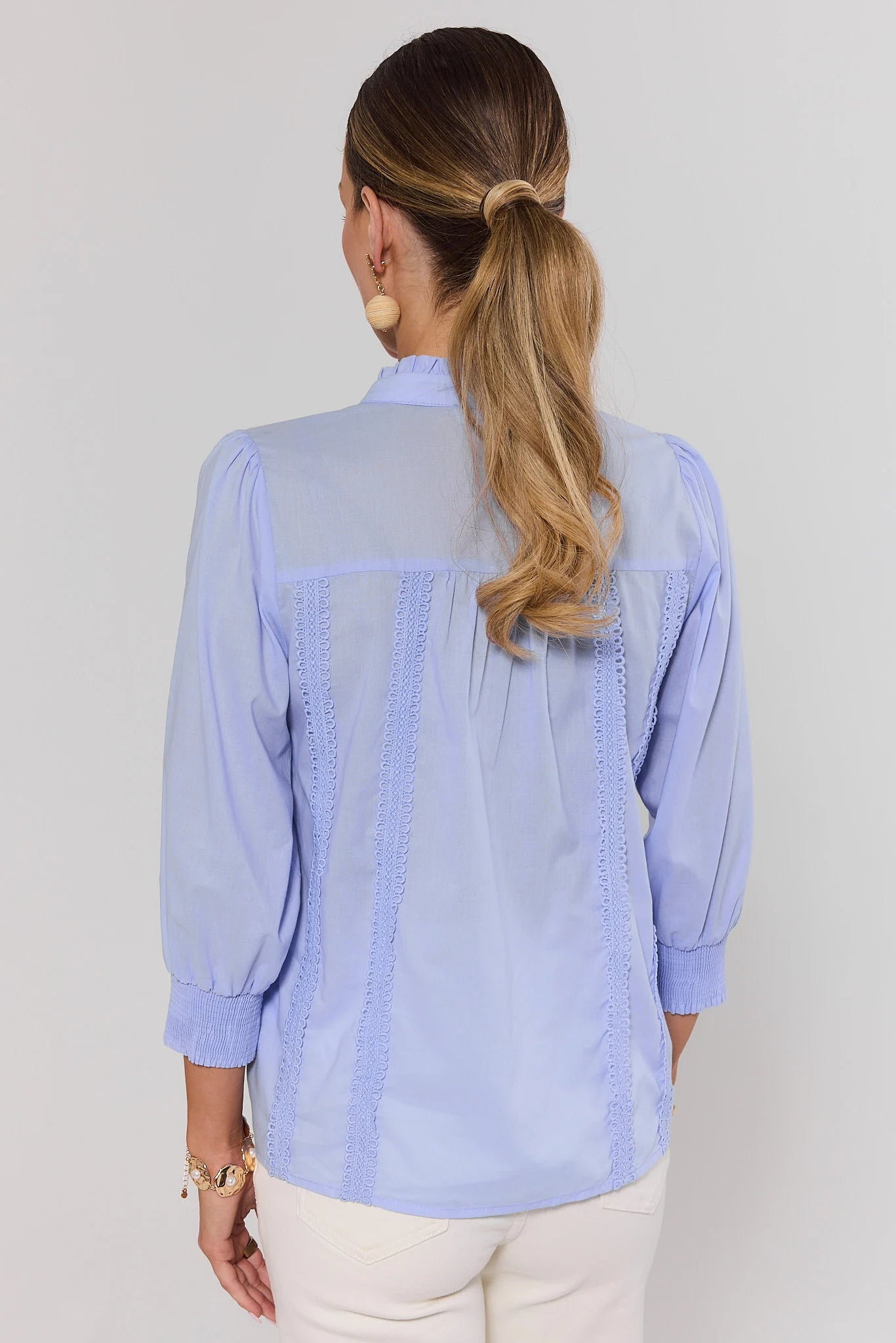 Woman standing wearing a light blue blouse with a plain background