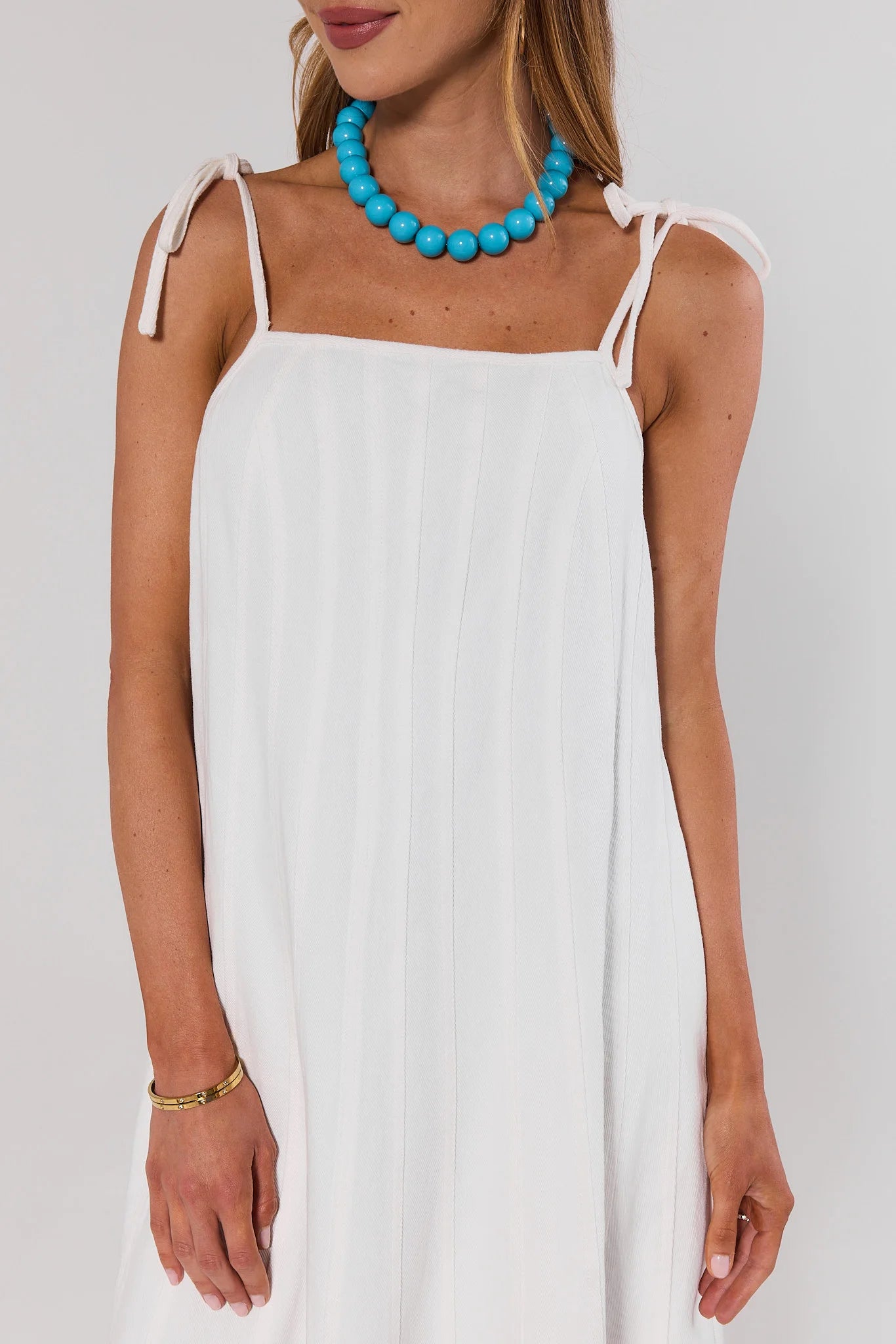 close up Woman wearing a white dress with thin straps and a blue necklace on a plain background