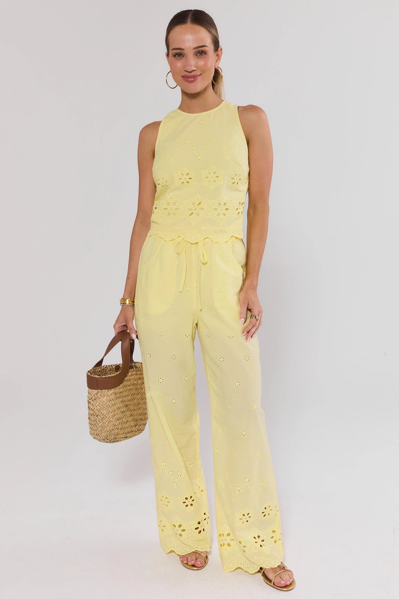 Woman wearing a yellow top and pants holding a straw bag on a white background