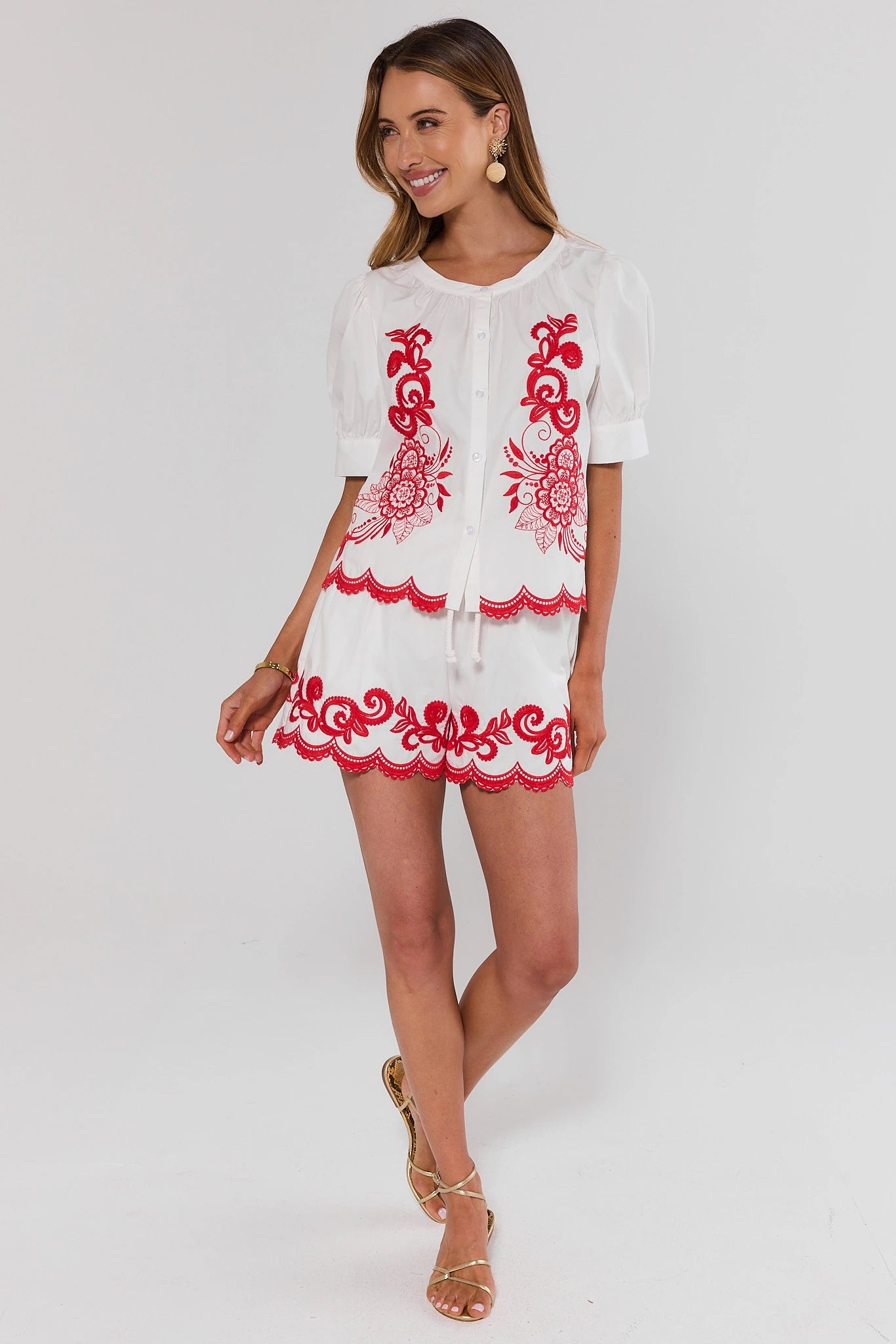 Woman wearing a white top and shorts with red embroidery on a white background