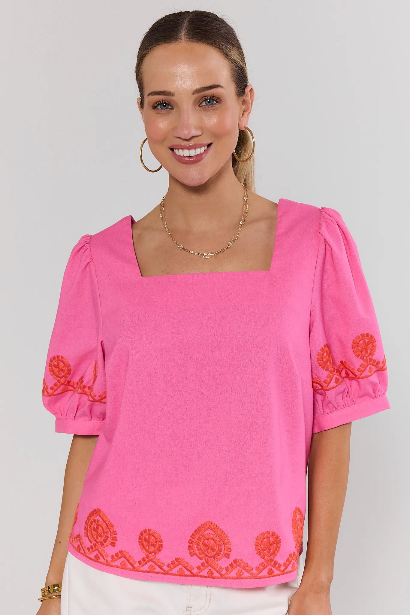 Woman wearing a pink blouse with orange embroidery on a gray background