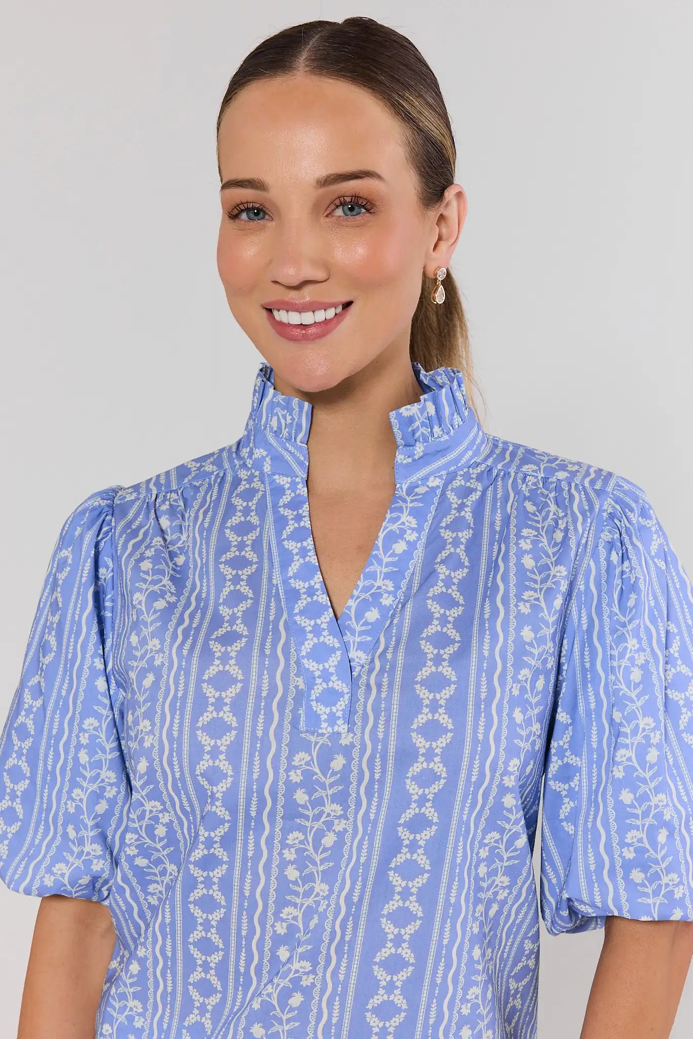 close up Woman wearing a blue patterned janet top against a plain background