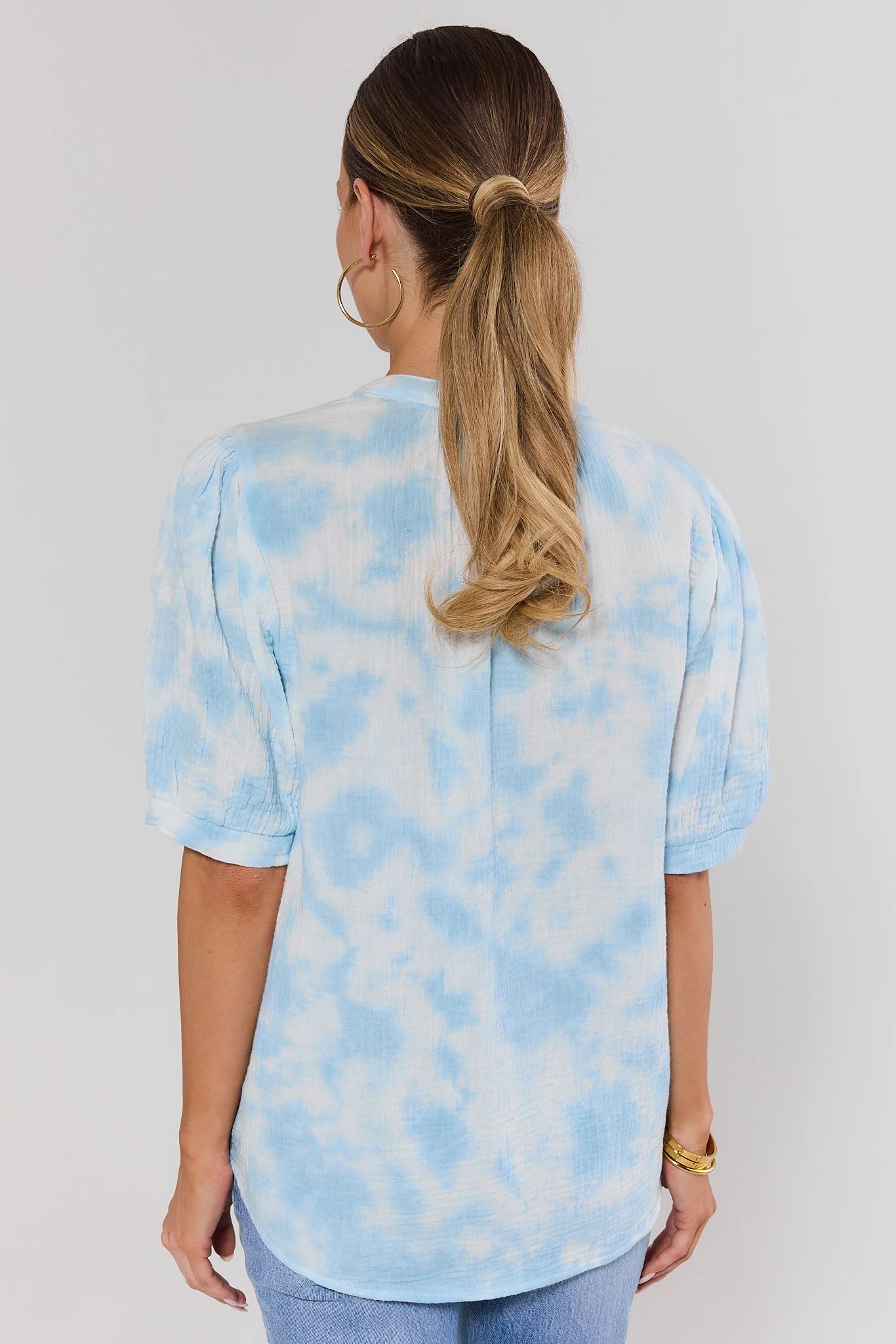 Woman wearing a light blue tie-dye shirt on a plain background standing