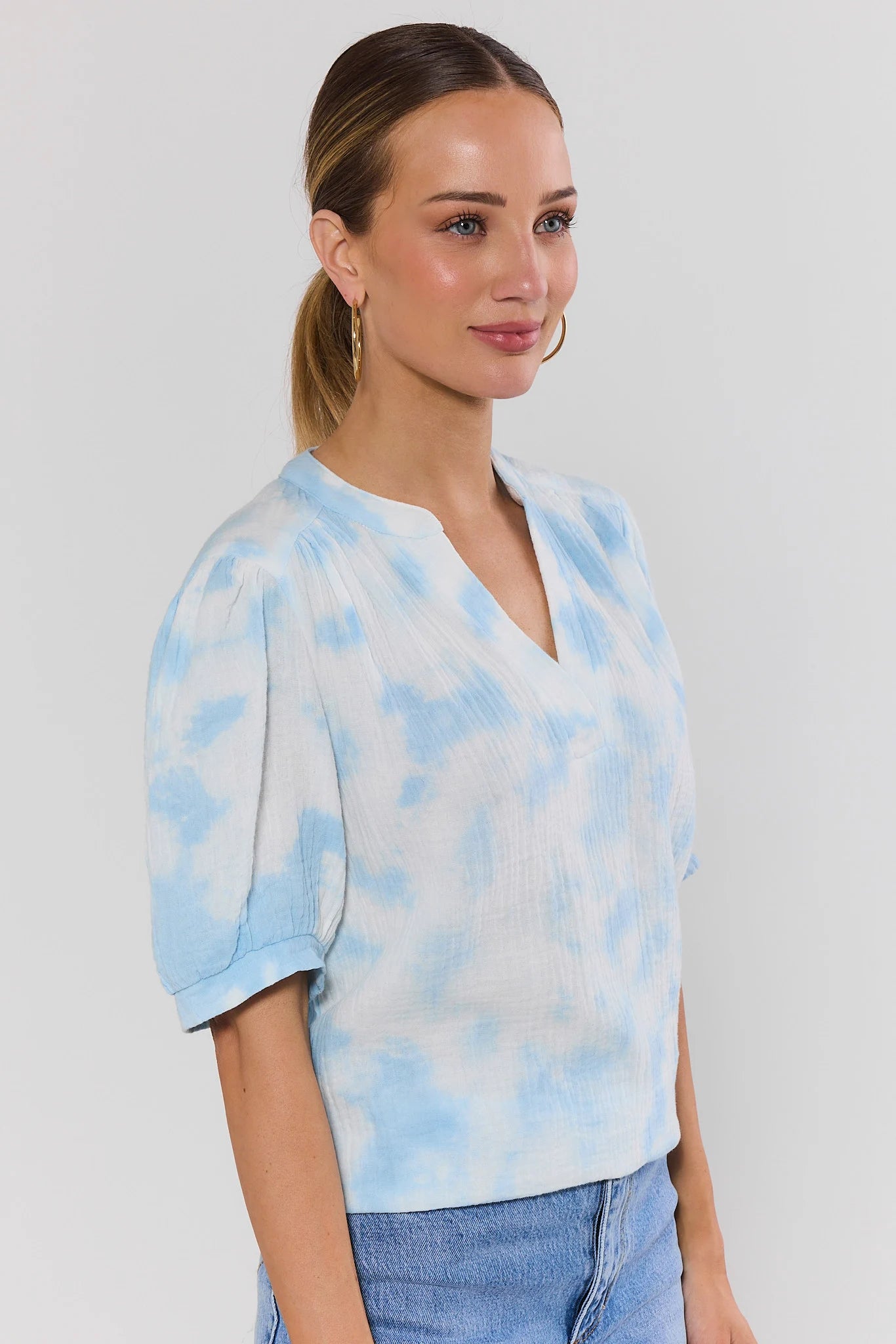 side shot Woman wearing a blue tie-dye shirt against a plain background