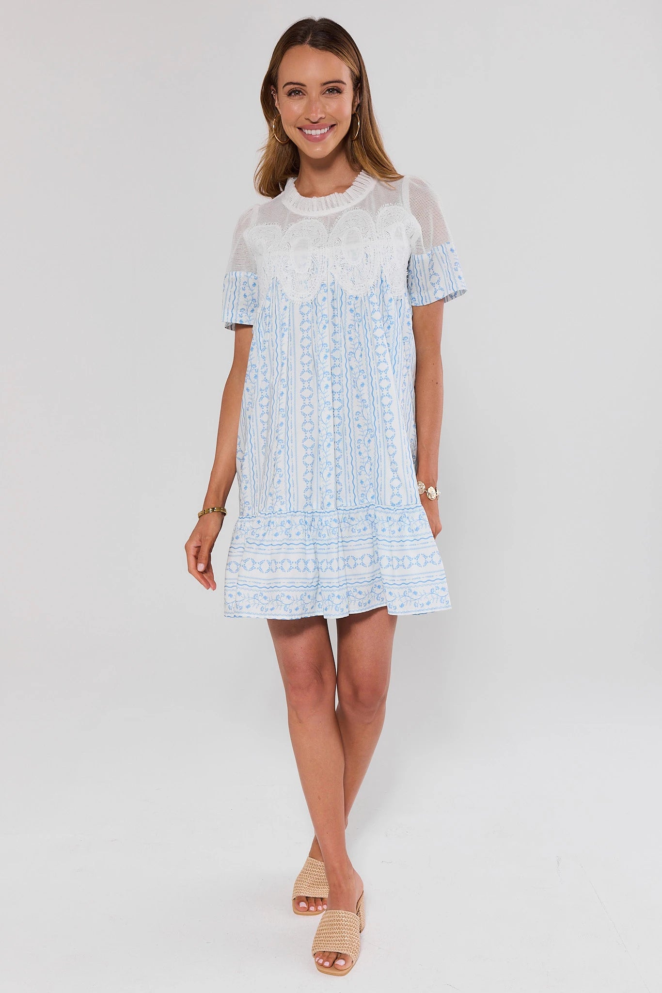 Woman wearing a light blue dress with white lace details on a white background standing