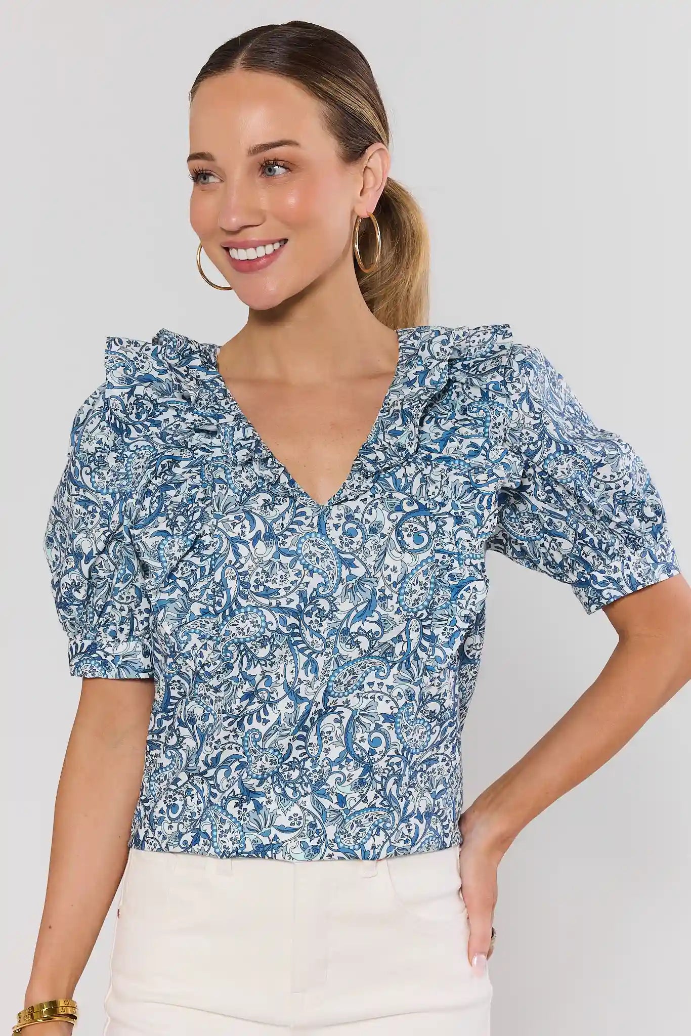 Woman wearing a blue floral paisley blouse against a plain background 