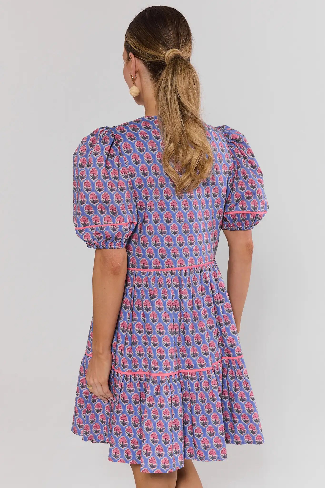 Woman wearing a blue patterned dress with puff sleeves on a plain background standing