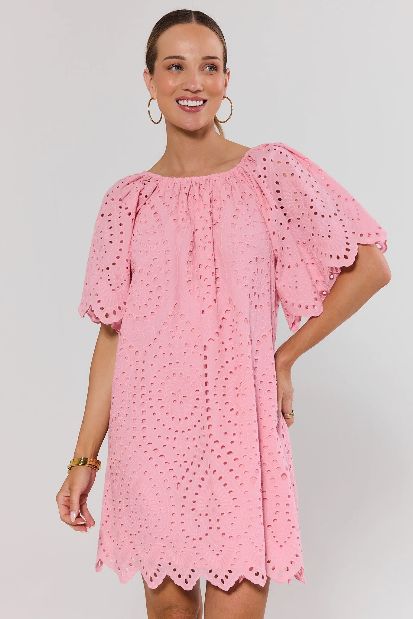 Woman wearing a pink eyelet dress against a plain background