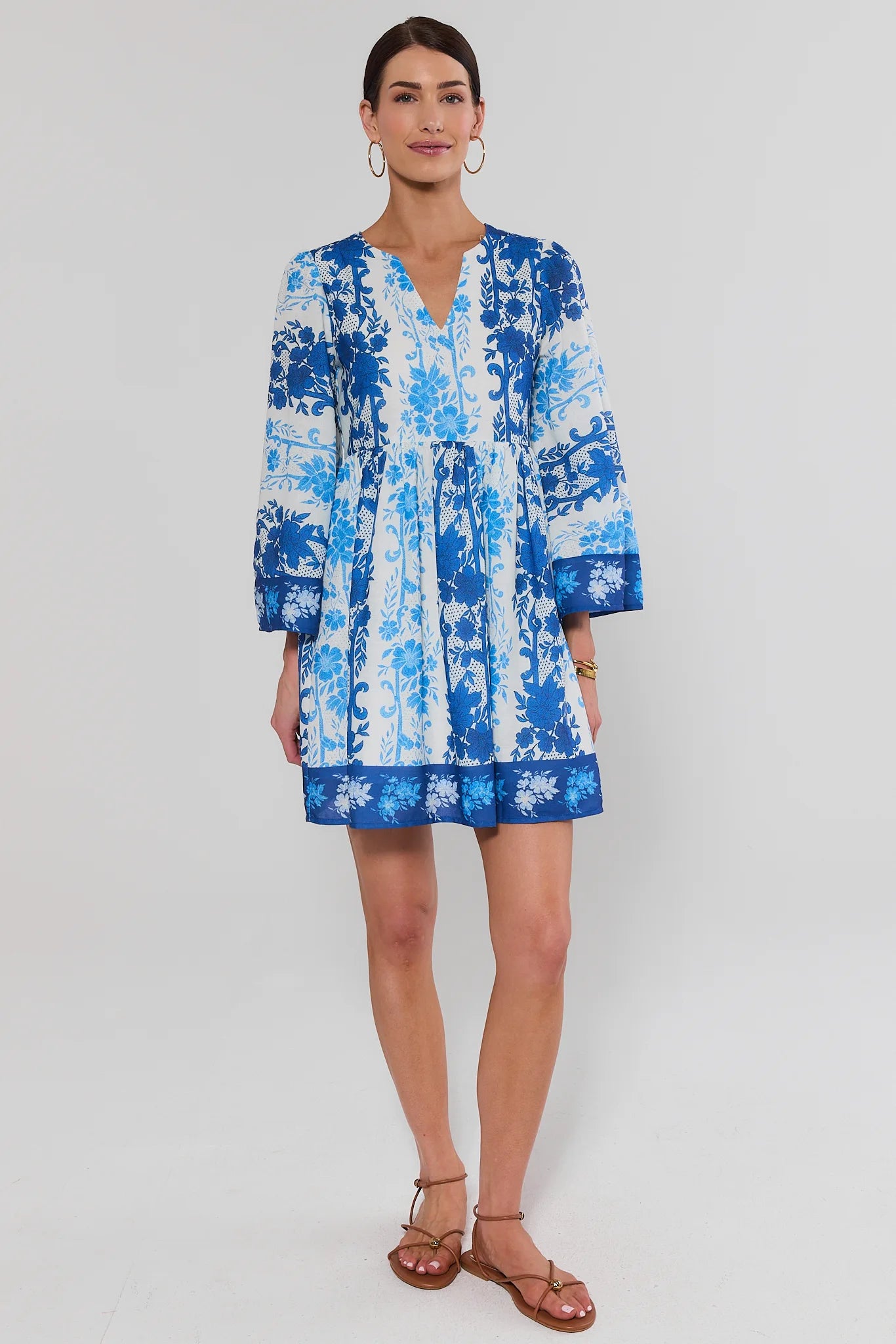 Woman wearing a blue and white patterned dress on a plain background standing 